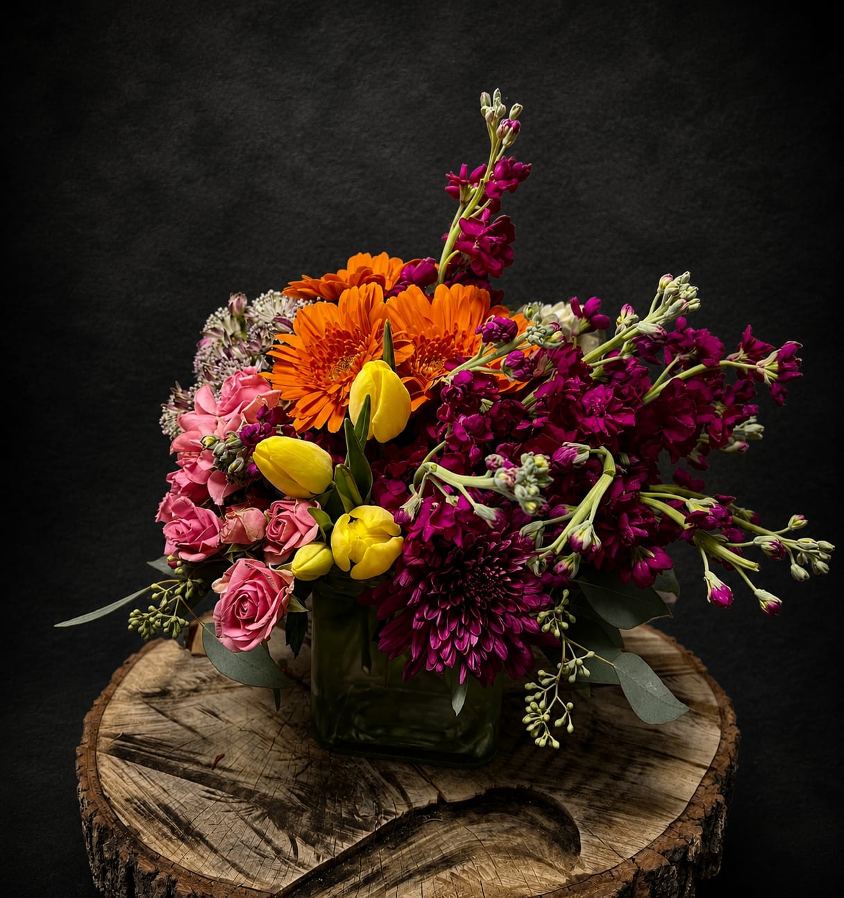 My Everything - Bright, joyful colors make this mixed flower arrangement feel like a little celebration in a square glass vase-perfect as an anniversary bouquet, birthday surprise, or Mother's Day gift. The vibrant mix of pink roses, deep magenta blooms, bright orange gerbera daisies and sunny yellow tulips reads as both romantic and playful, so the person you're thinking of will feel truly seen whether you're saying "I love you," "get well soon," or "thank you."  This compact, garden-style design is densely layered for a lush look, with airy stock and chrysanthemum accents adding movement and texture around the rounded clusters of carnations, hydrangea-like fillers and tulips. Arranged low in a clear square glass vase, it presents a full, overflowing face of mixed color that works well on mantels, desks, or a dining table centerpiece.  Ideal for spring and summer occasions-or any Just Because moment-this bouquet also suits housewarmings, retirements, apologies, and thinking-of-you notes. The arrangement arrives ready to display; keep flowers in fresh water, recut stems every few days, and place away from direct heat to extend enjoyment.