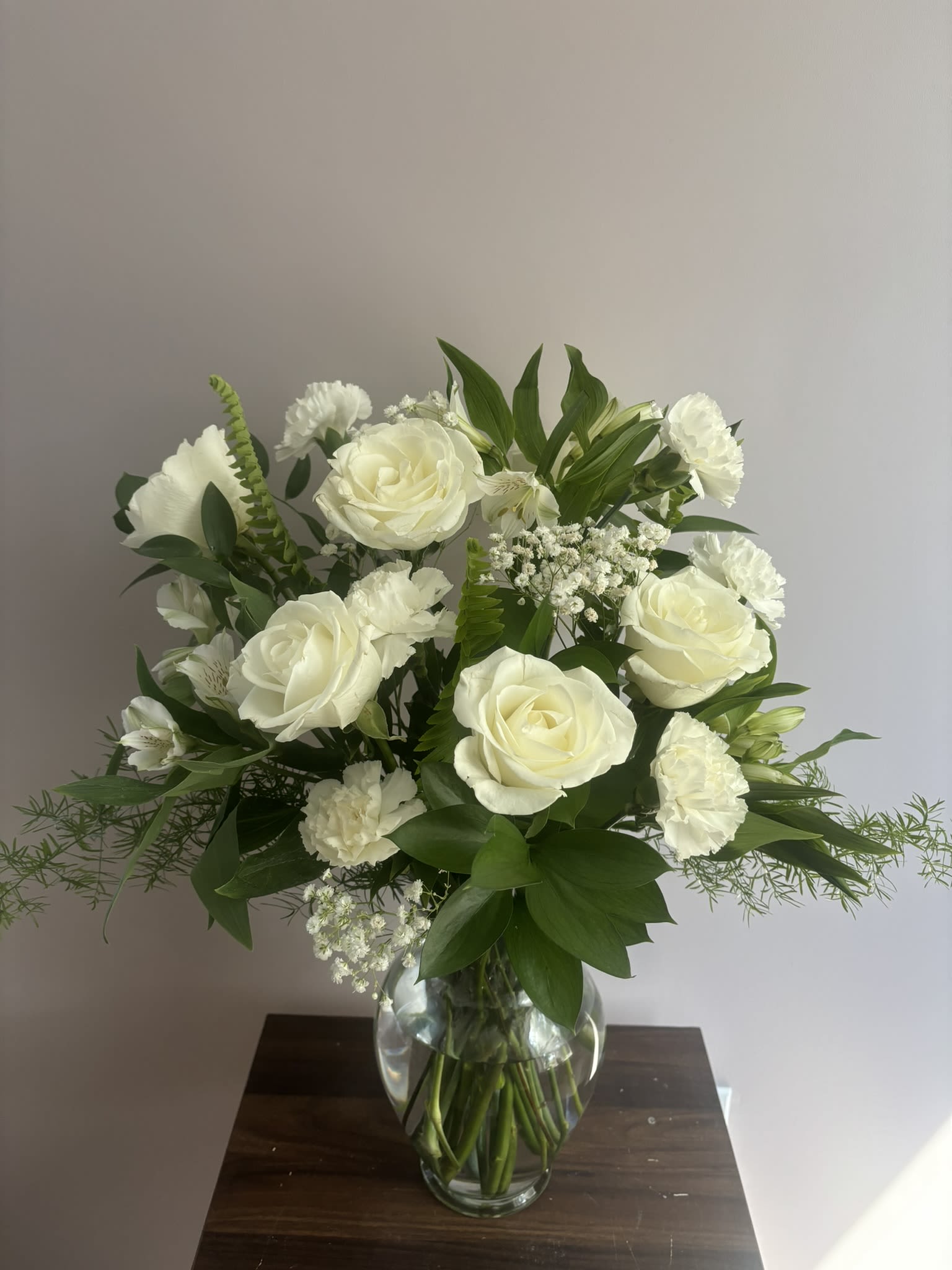 White roses and carnations arranged in a clear glass vase