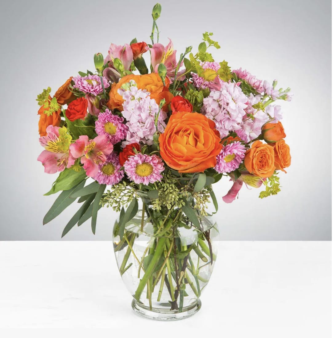 Mixed bouquet of orange and pink flowers in a clear glass vase