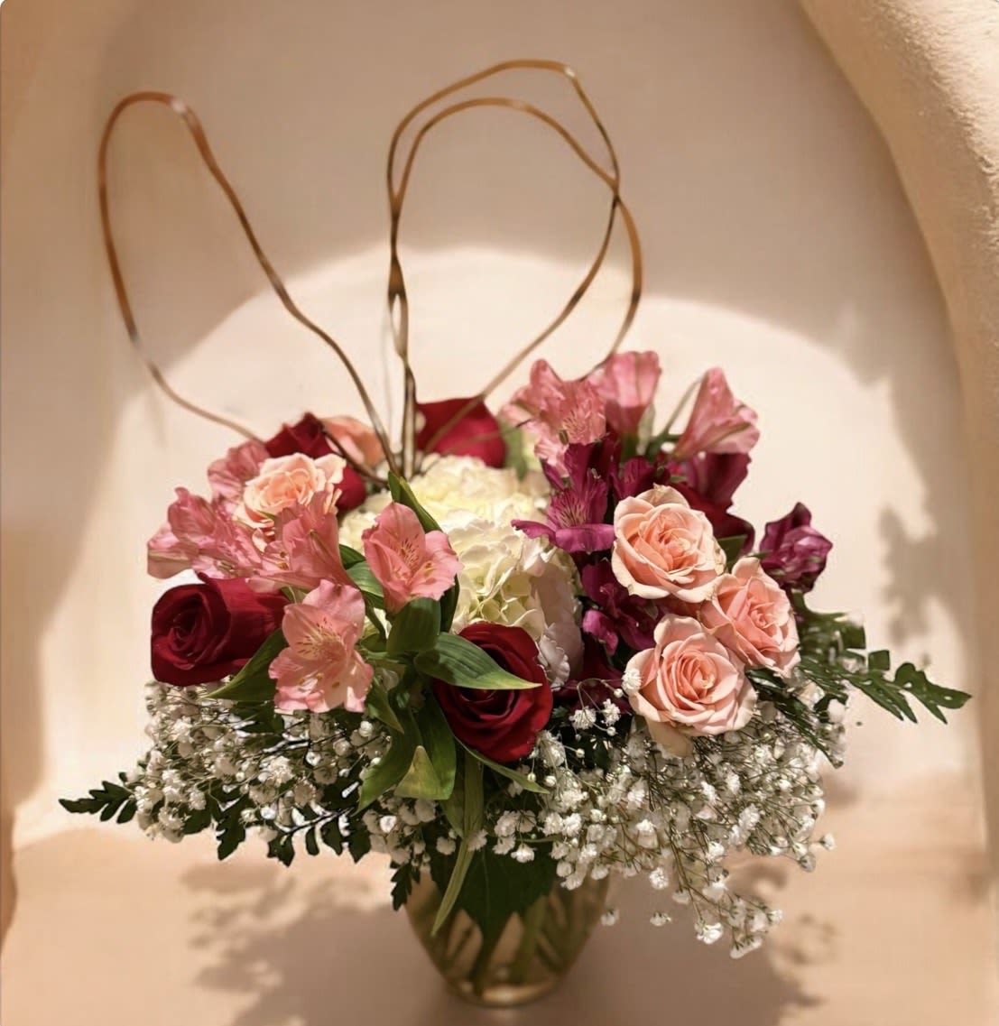 Blush Me Forever - Delicate, romantic, and endlessly captivating, Blush me Forever is a love story told in soft petals and graceful movement. Blush and berry-toned roses are paired with creamy hydrangea, airy baby’s breath, and elegant alstroemeria, all artfully finished with sculptural looping foliage for a refined, modern silhouette.  Designed to evoke intimacy and devotion, this arrangement is perfect for Valentine’s Day gestures that feel personal, luxurious, and unforgettable. Presented in a clear glass vase, Blush Me Forever is timeless romance with a contemporary soul.  A soft, romantic expression of love designed to linger long after Valentine’s Day.