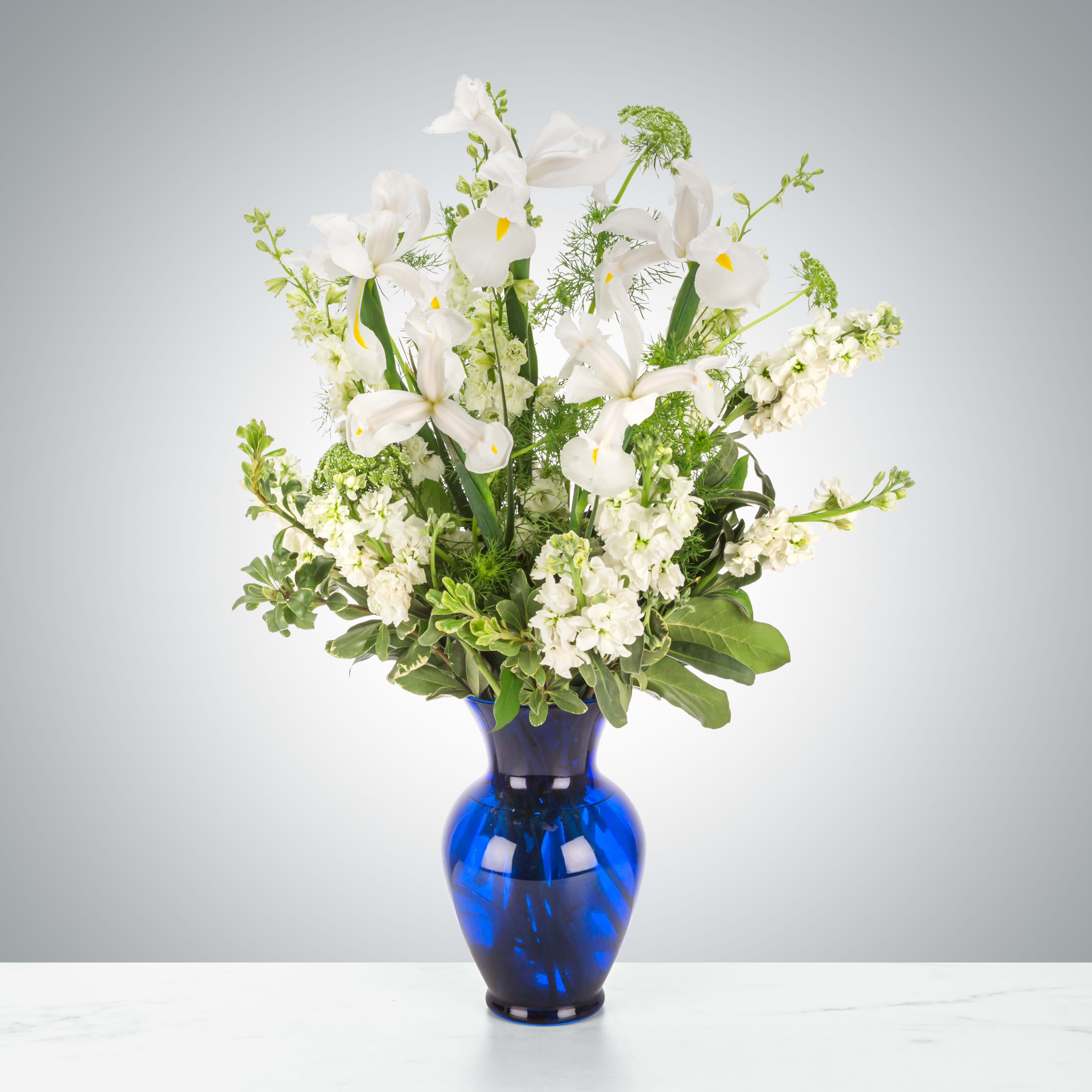 Crystal Symphony by BloomNation™ - This arrangement includes white iris, white stock, white snapdragons, and queen anne's lace in a blue vase. Send your condolences with Crystal Symphony by BloomNation™.