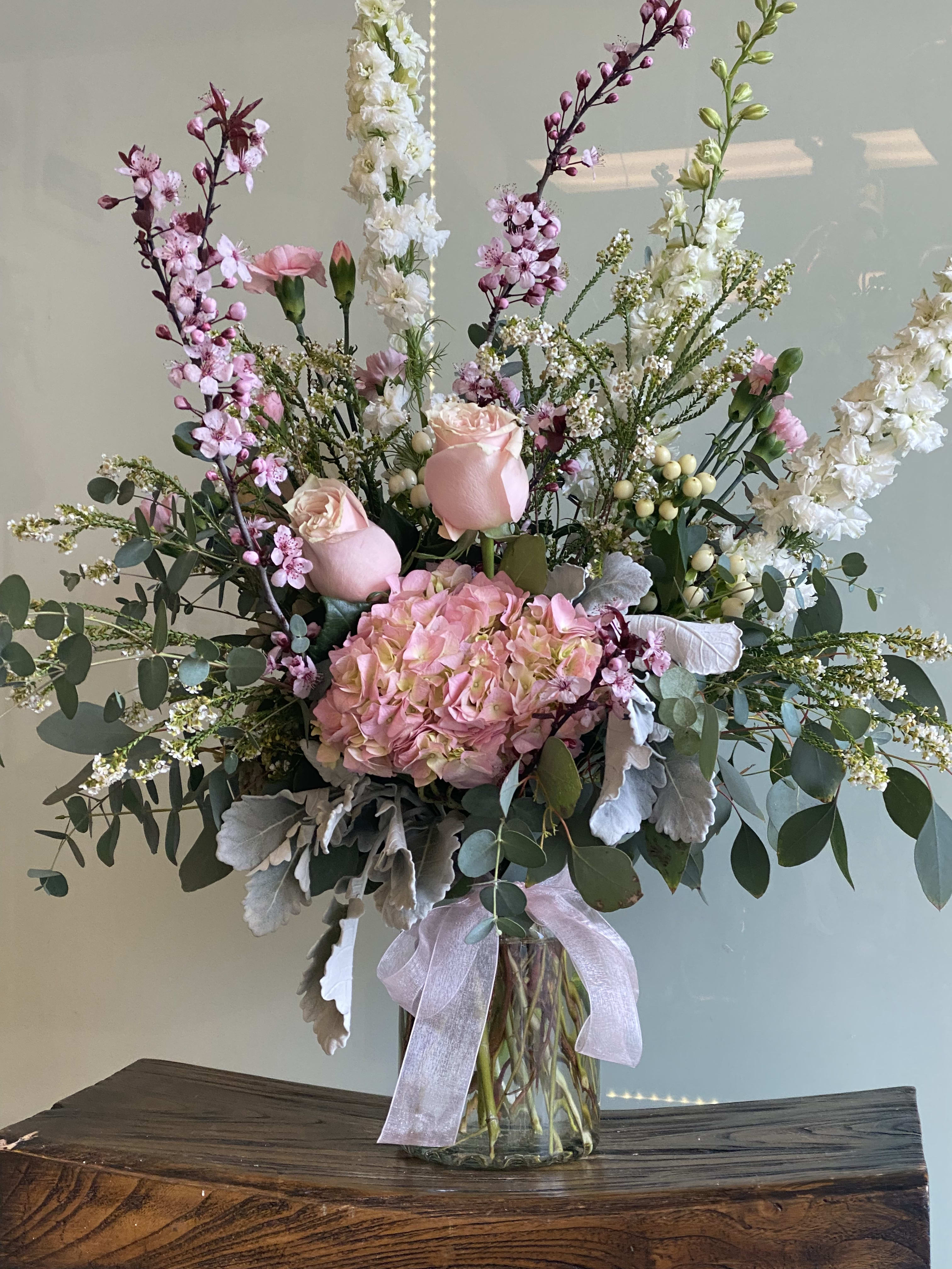Tall pink and white floral arrangement in a glass vase with a ribbon