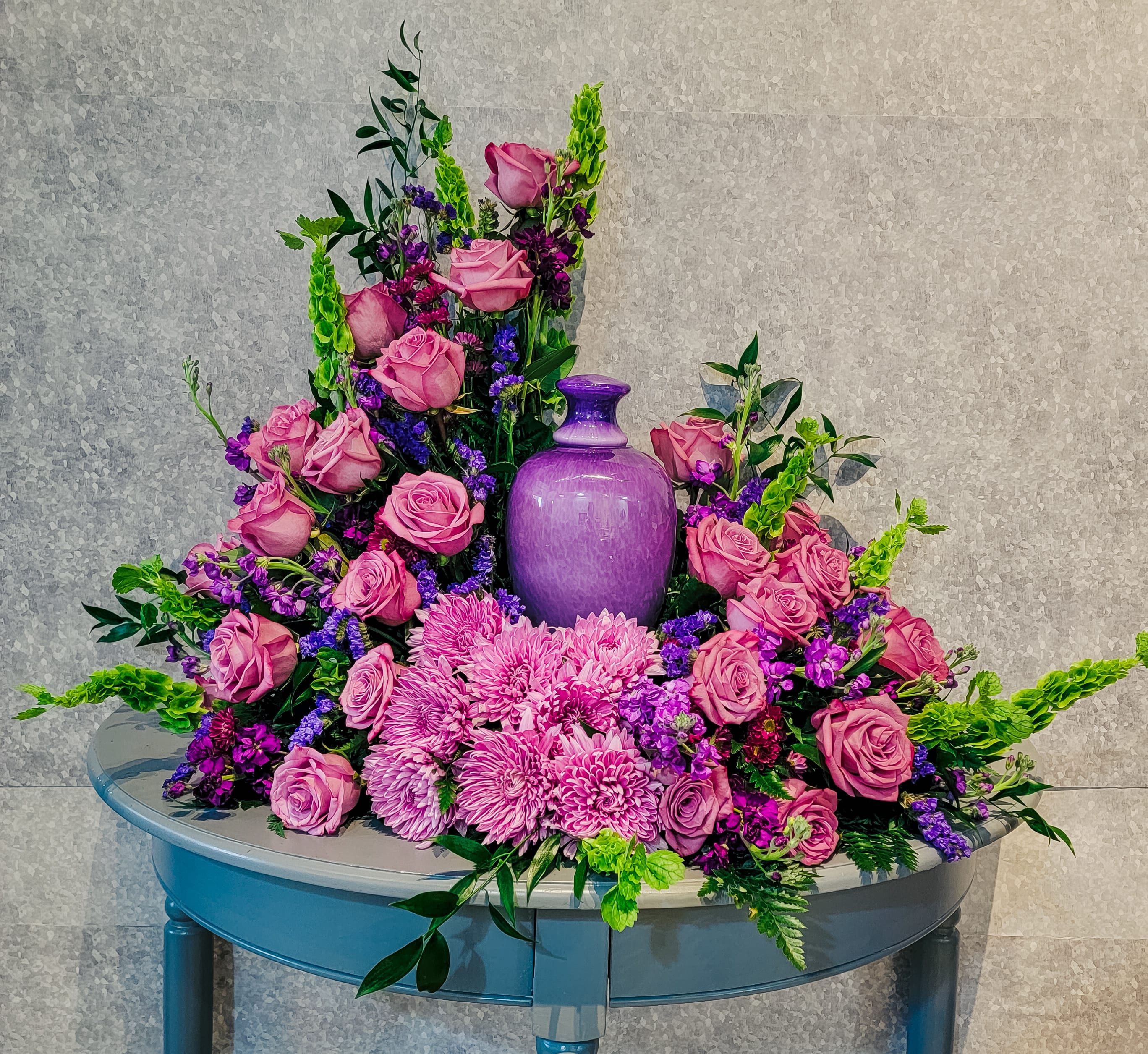 Pink roses and purple flowers arranged around a purple vase on a table