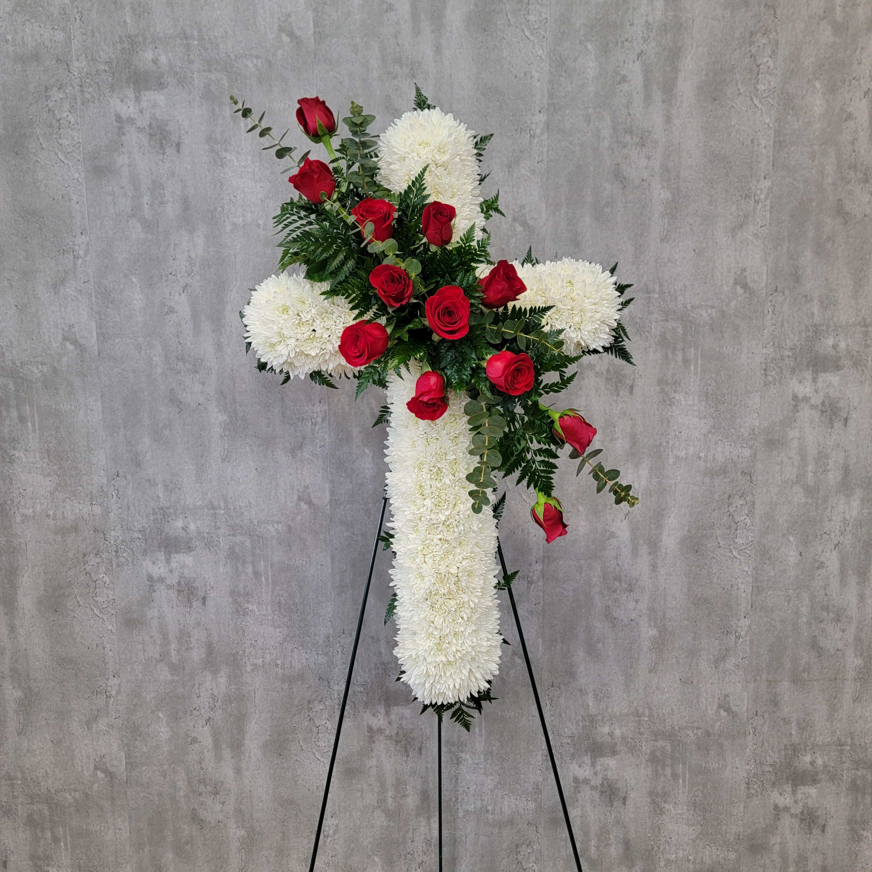 White floral cross with red roses on a stand