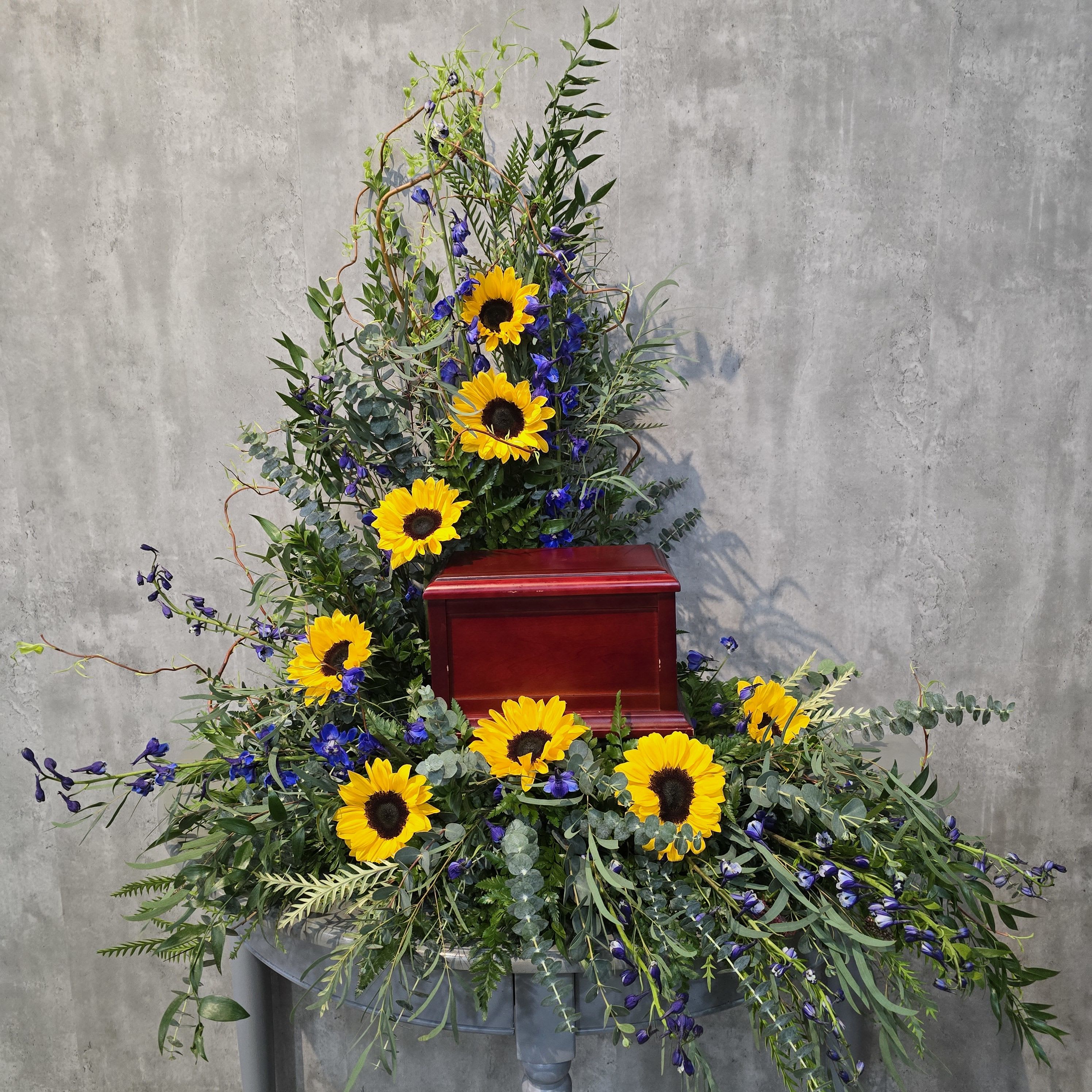 Sunflower funeral spray around a red urn on a pedestal