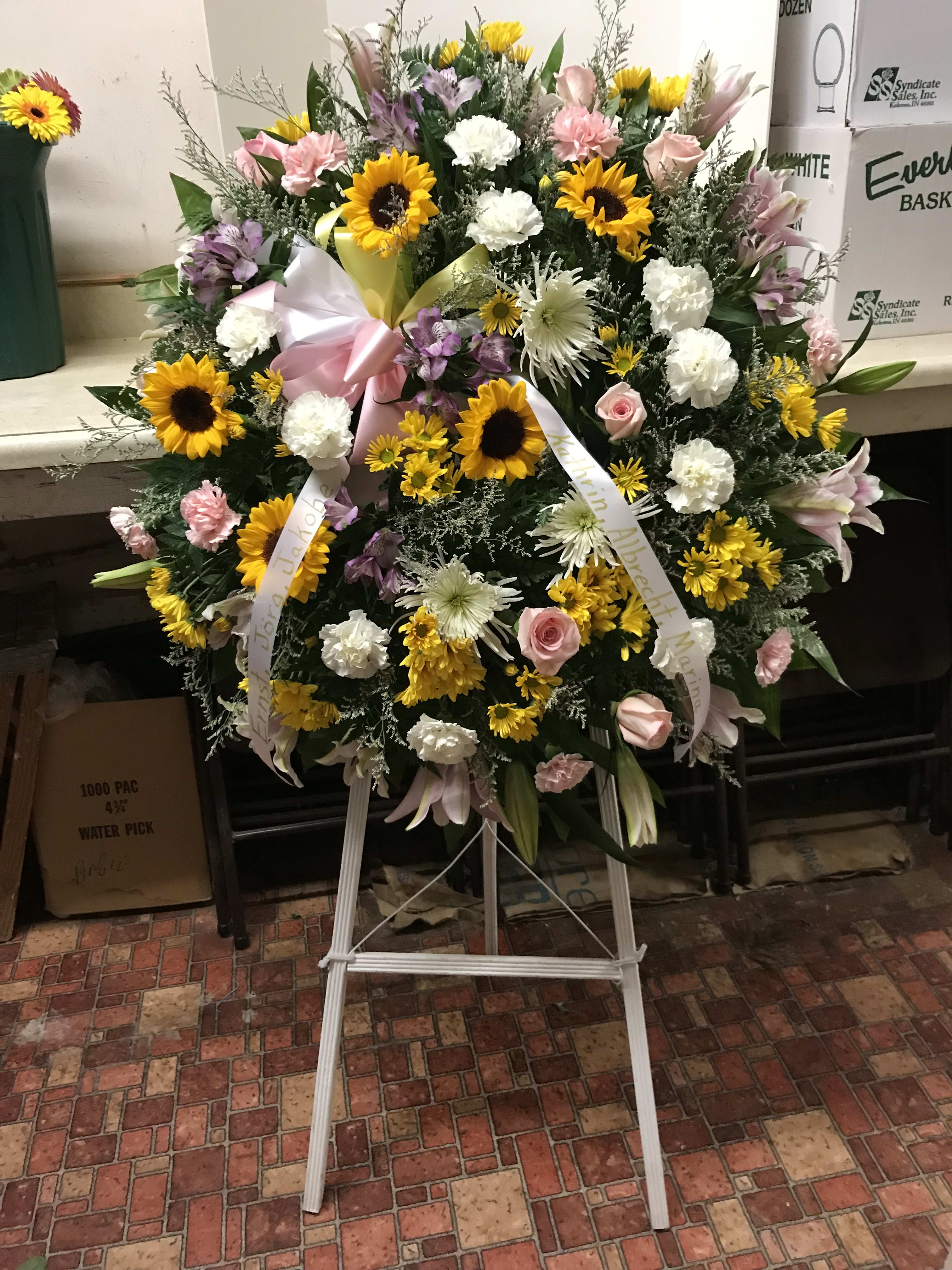 Large standing floral wreath with sunflowers, pink roses, and white blooms on an easel