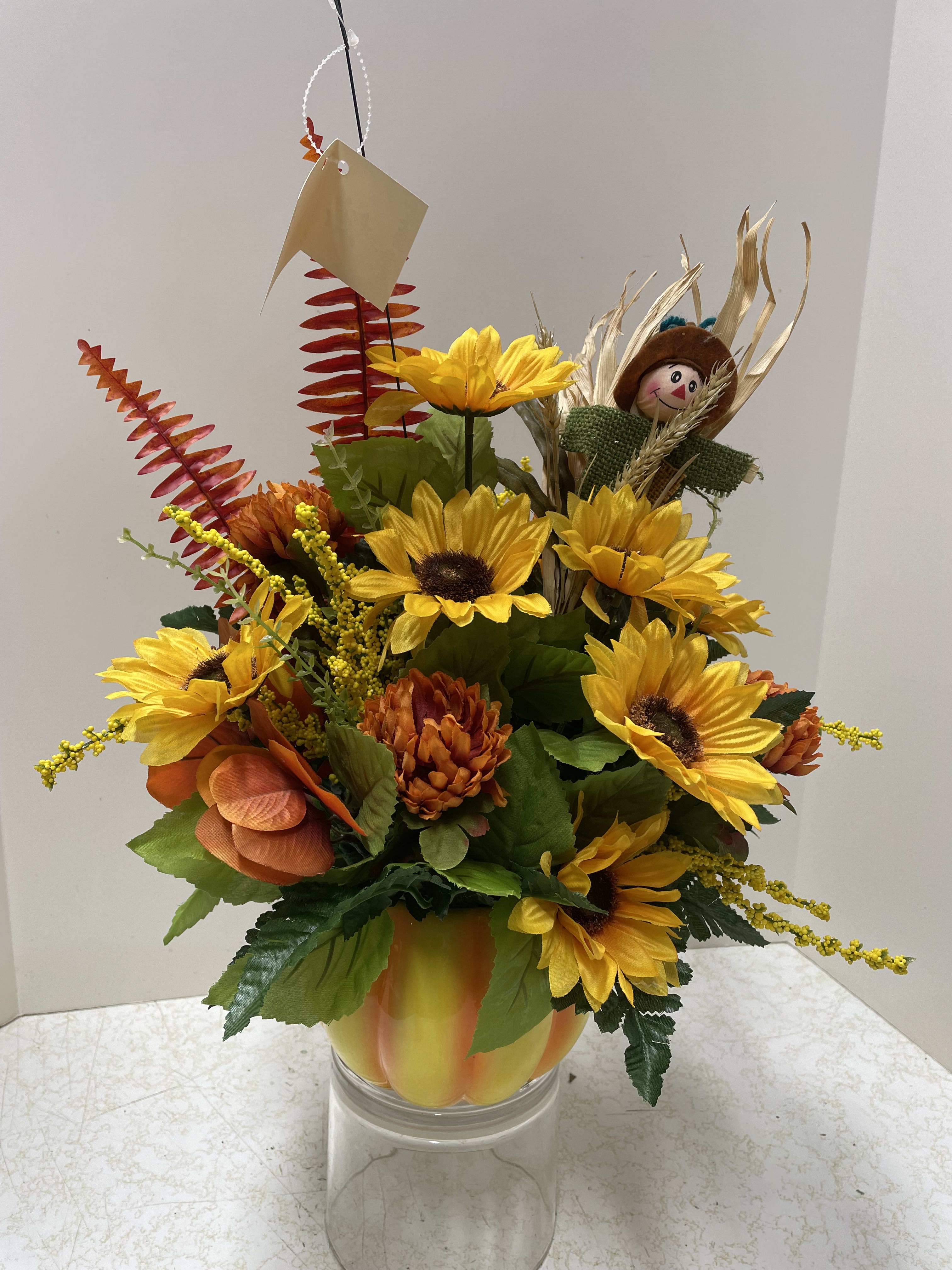 Sunflower arrangement in a clear glass vase with a small scarecrow pick