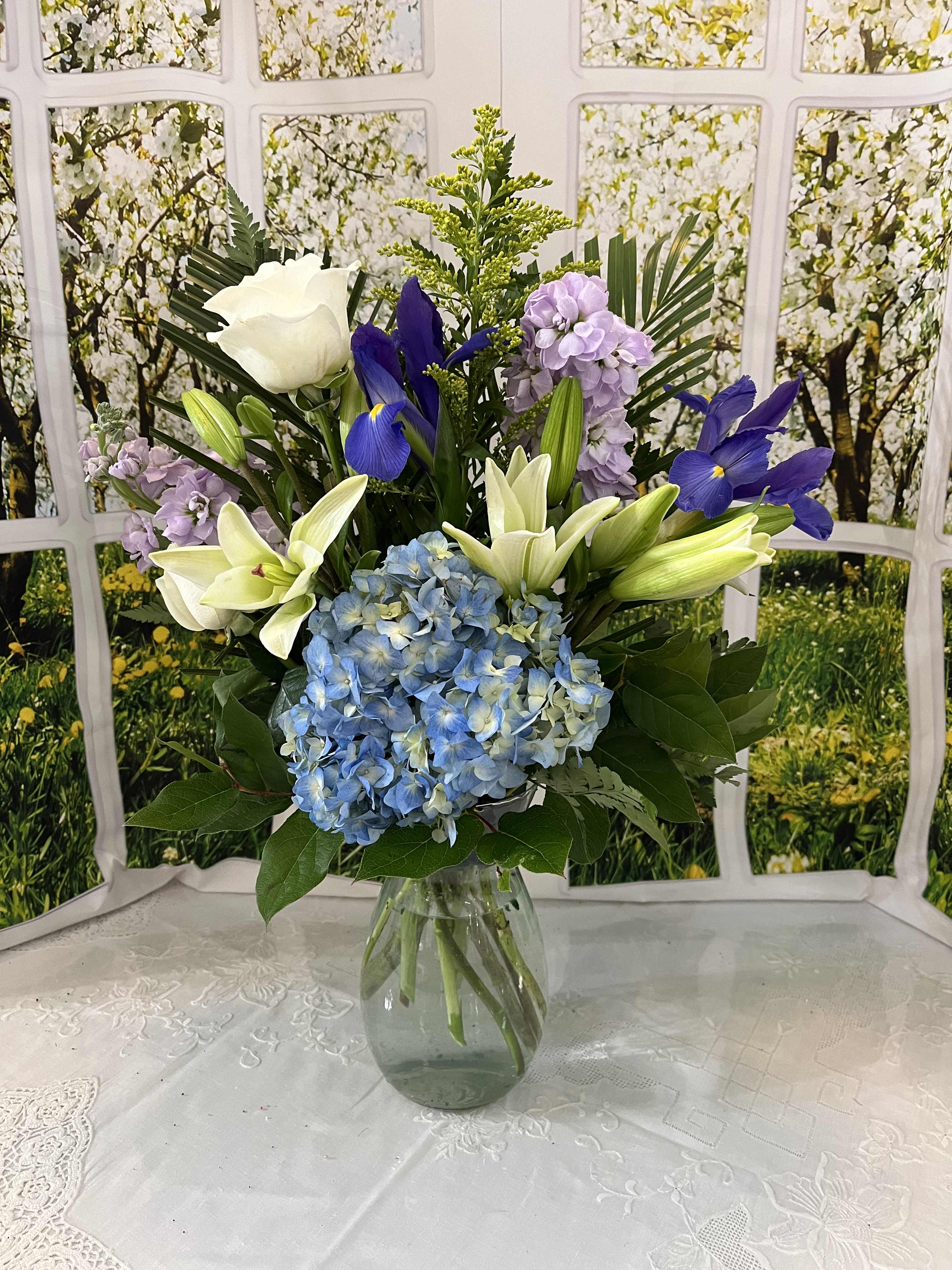 Bouquet of blue hydrangeas, white lilies, and purple flowers in a glass vase