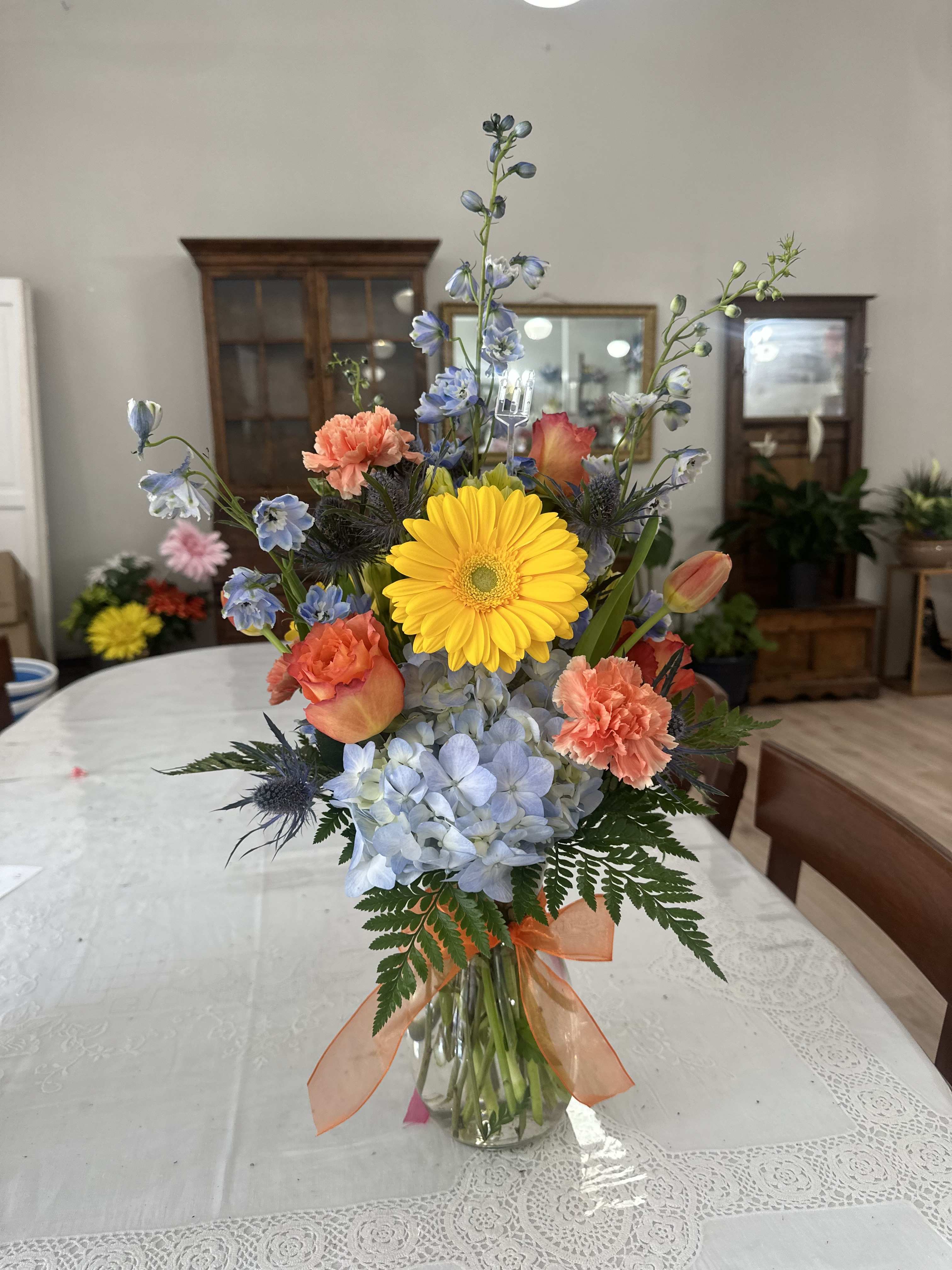 Mixed bouquet in a glass vase with yellow gerbera, blue hydrangea, and orange carnations