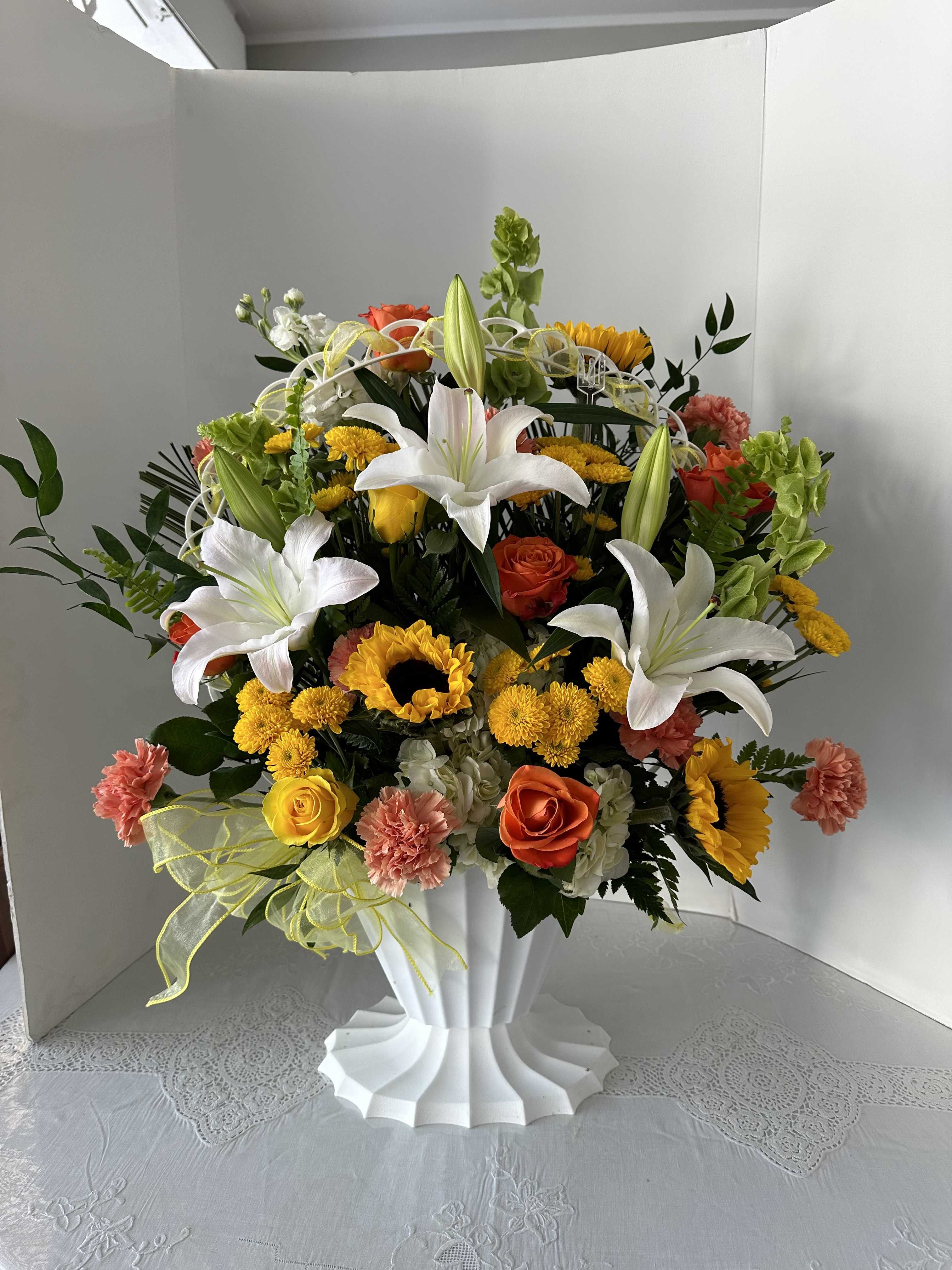 Large mixed bouquet with white lilies, roses, sunflowers, and carnations in a white vase