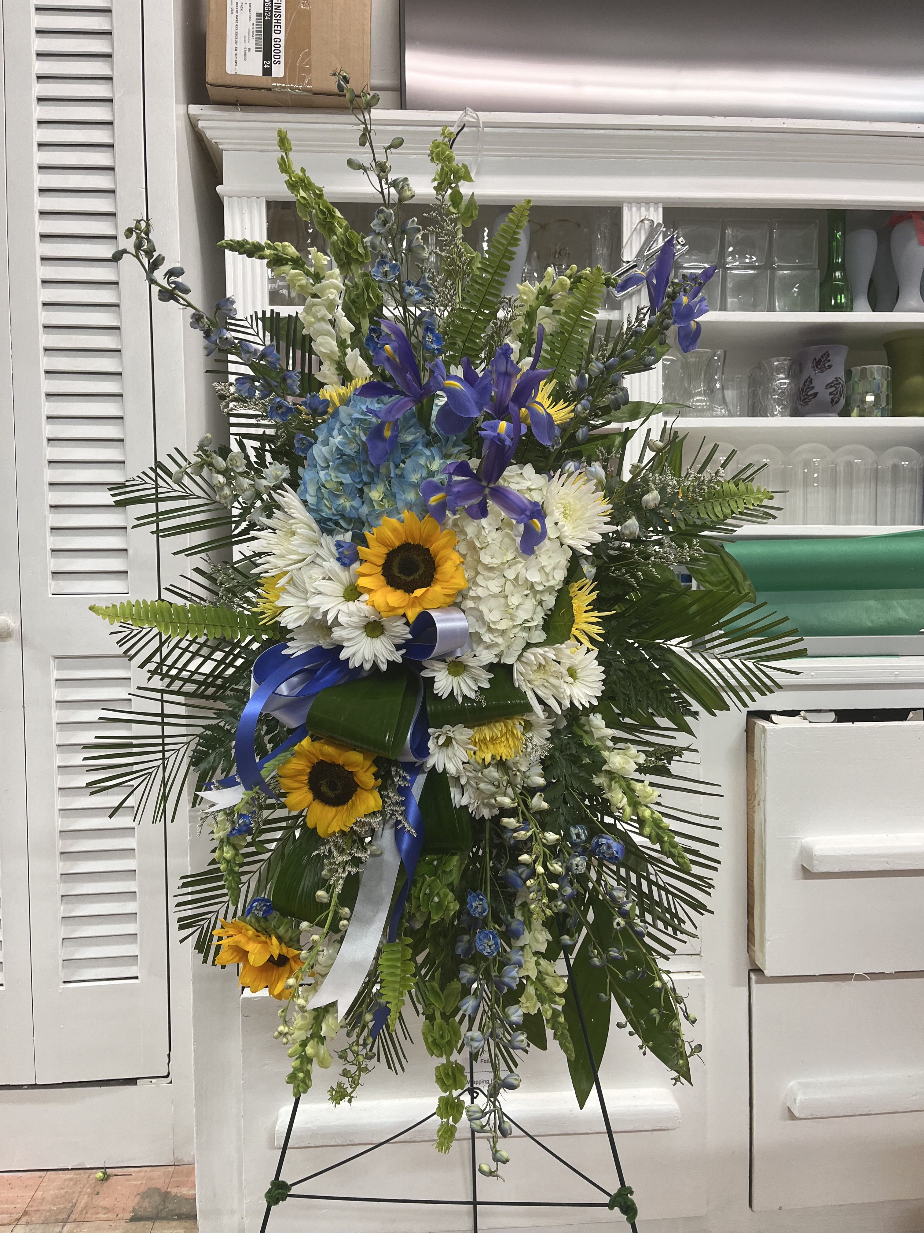 Tall standing floral spray with sunflowers, white daisies, and blue flowers