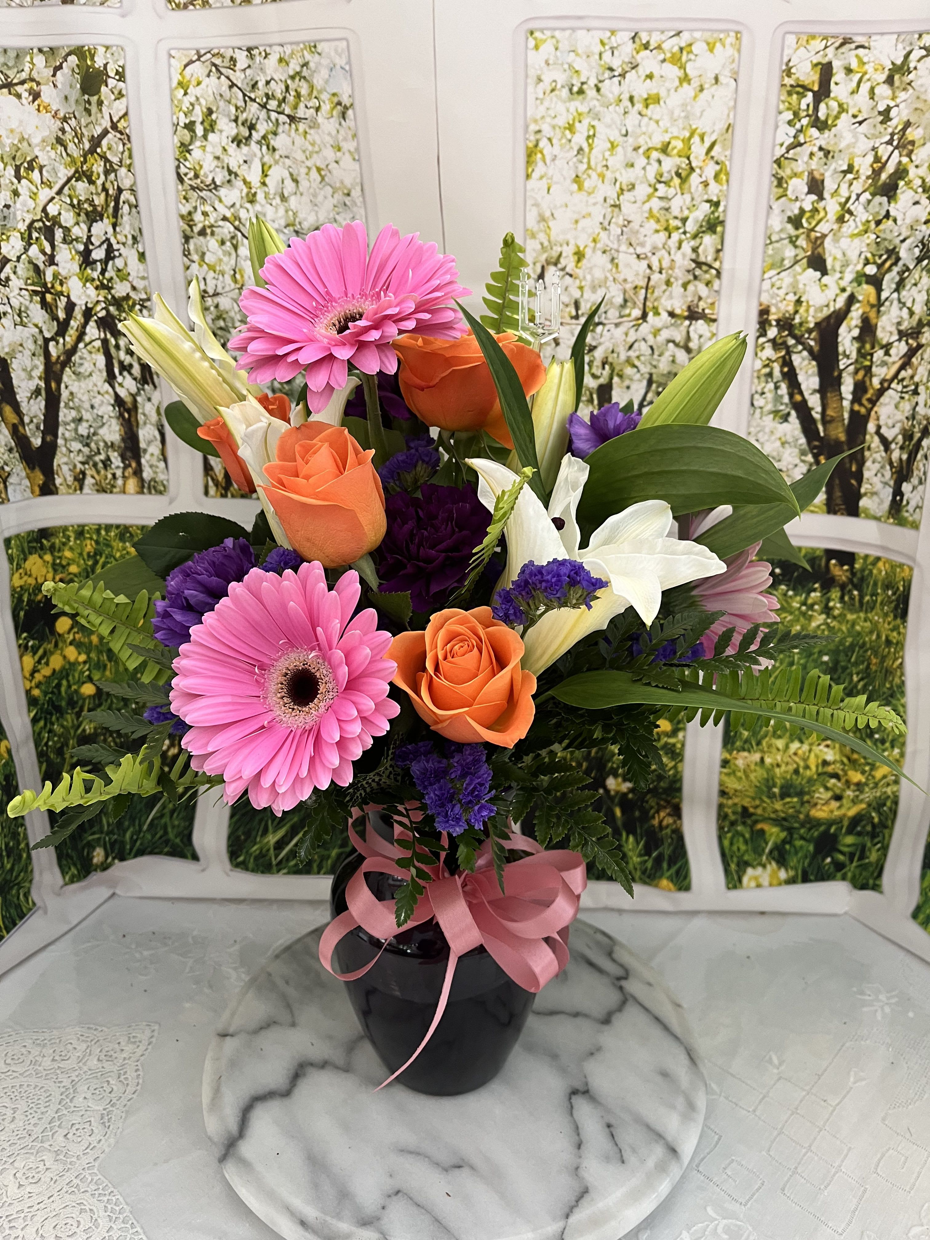 Bouquet of pink gerbera daisies, orange roses, and white lilies in a black vase