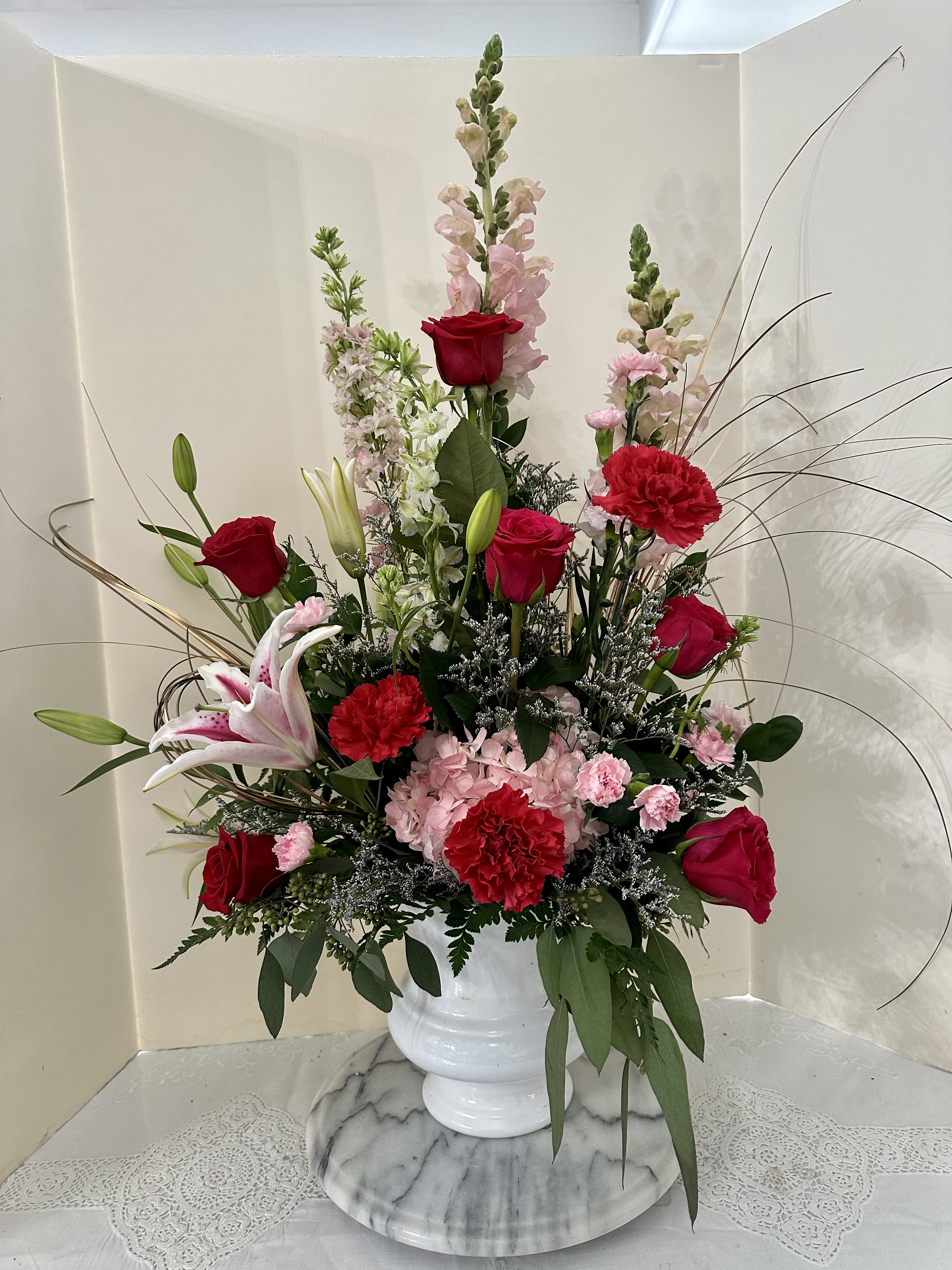 Tall bouquet of red roses, pink lilies, and carnations in a white vase