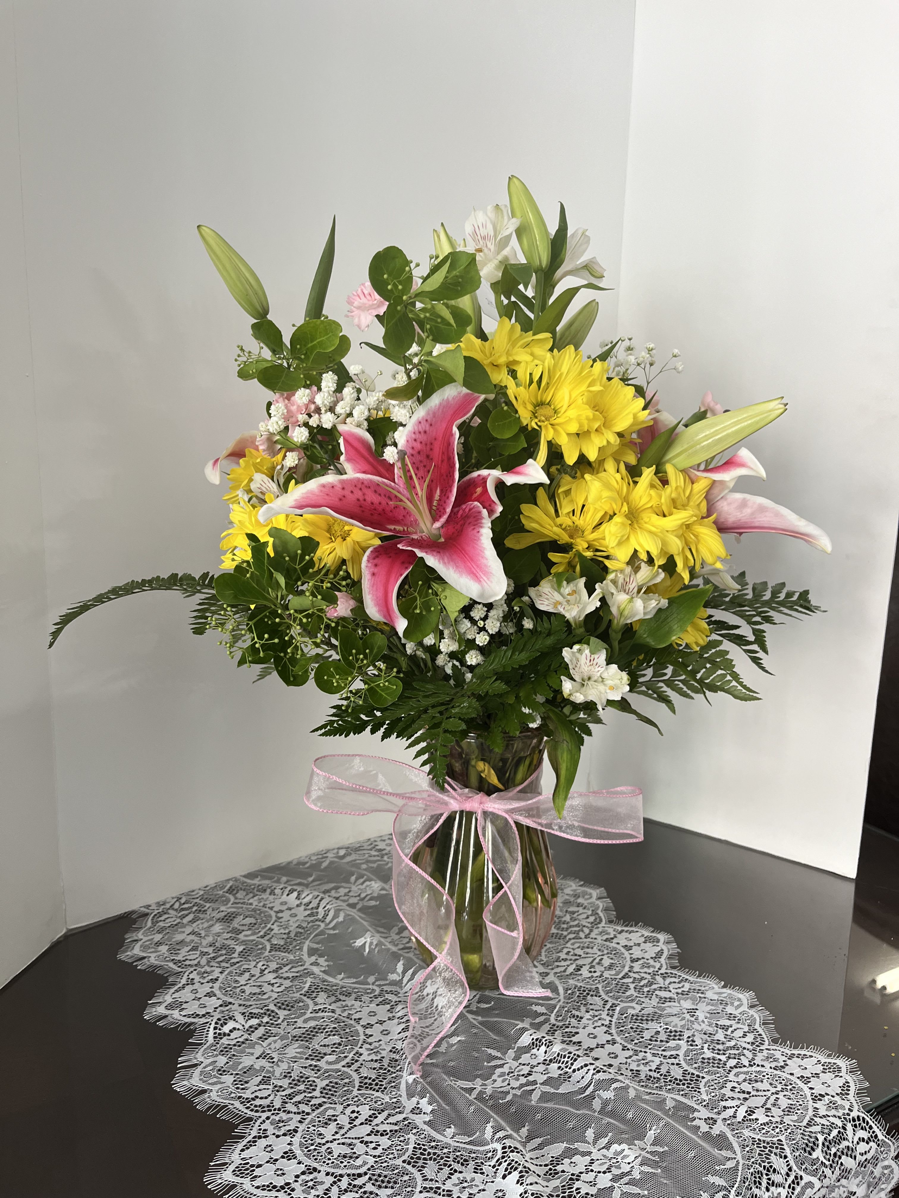 Pink lilies and yellow daisies in a glass vase with a pink ribbon