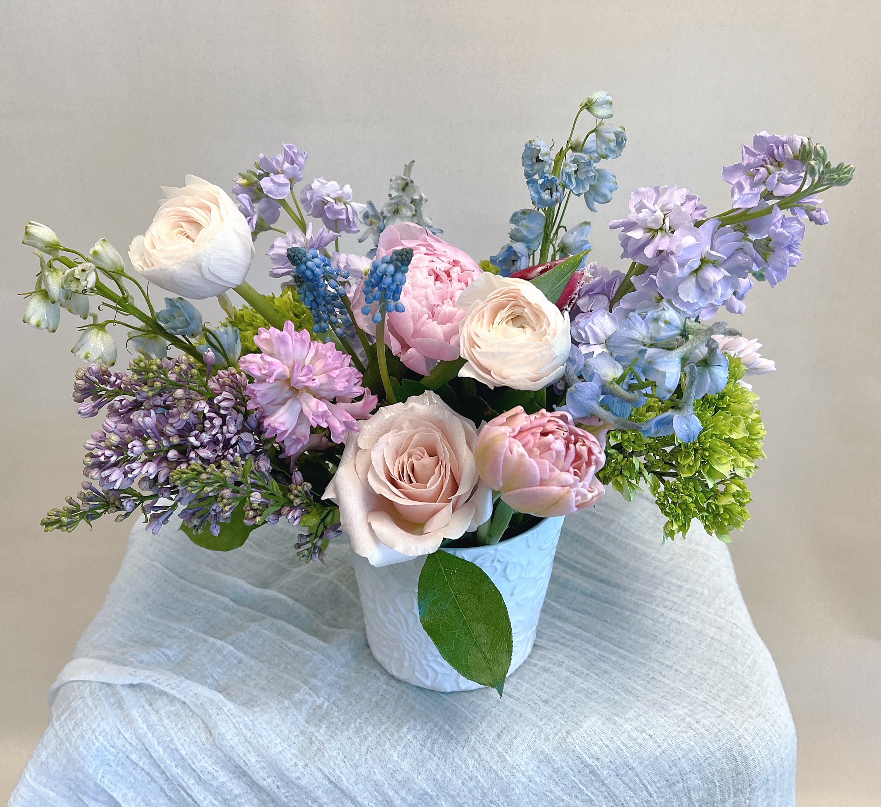 Pastel bouquet of roses, peonies, and blue-purple blooms in a white vase