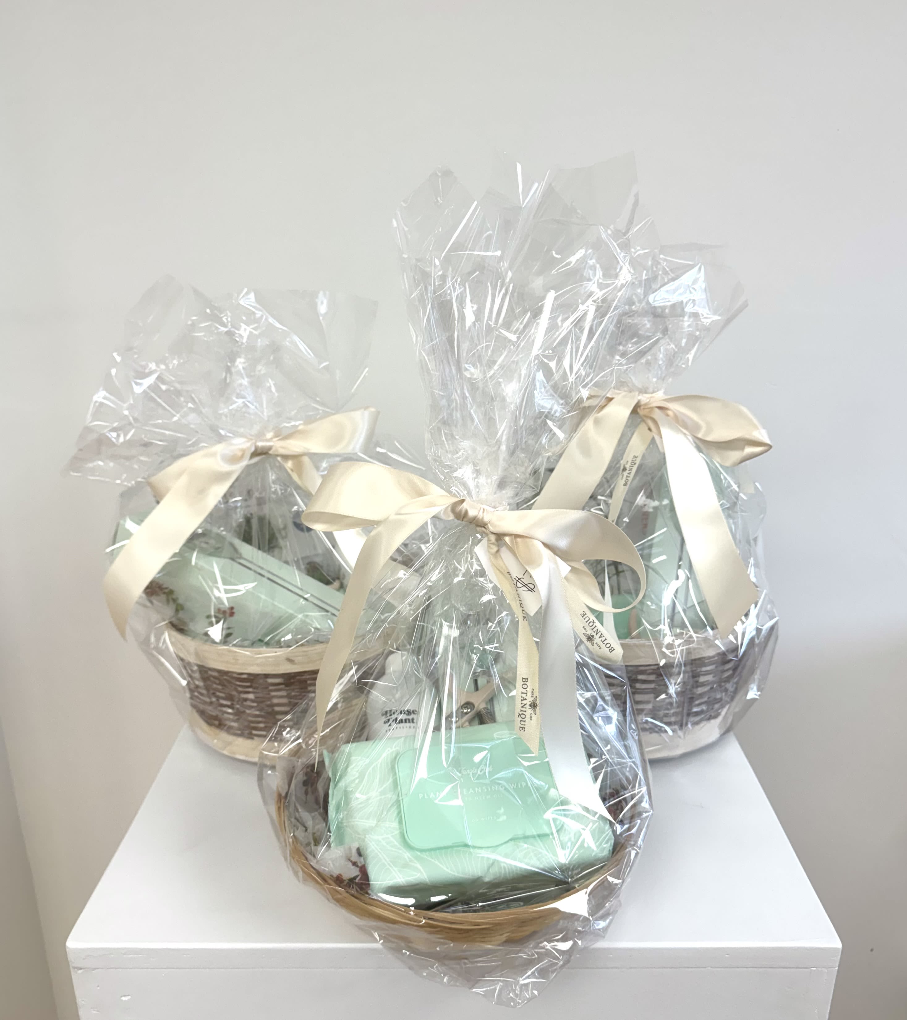 Three wrapped gift baskets with cream ribbons on a white surface