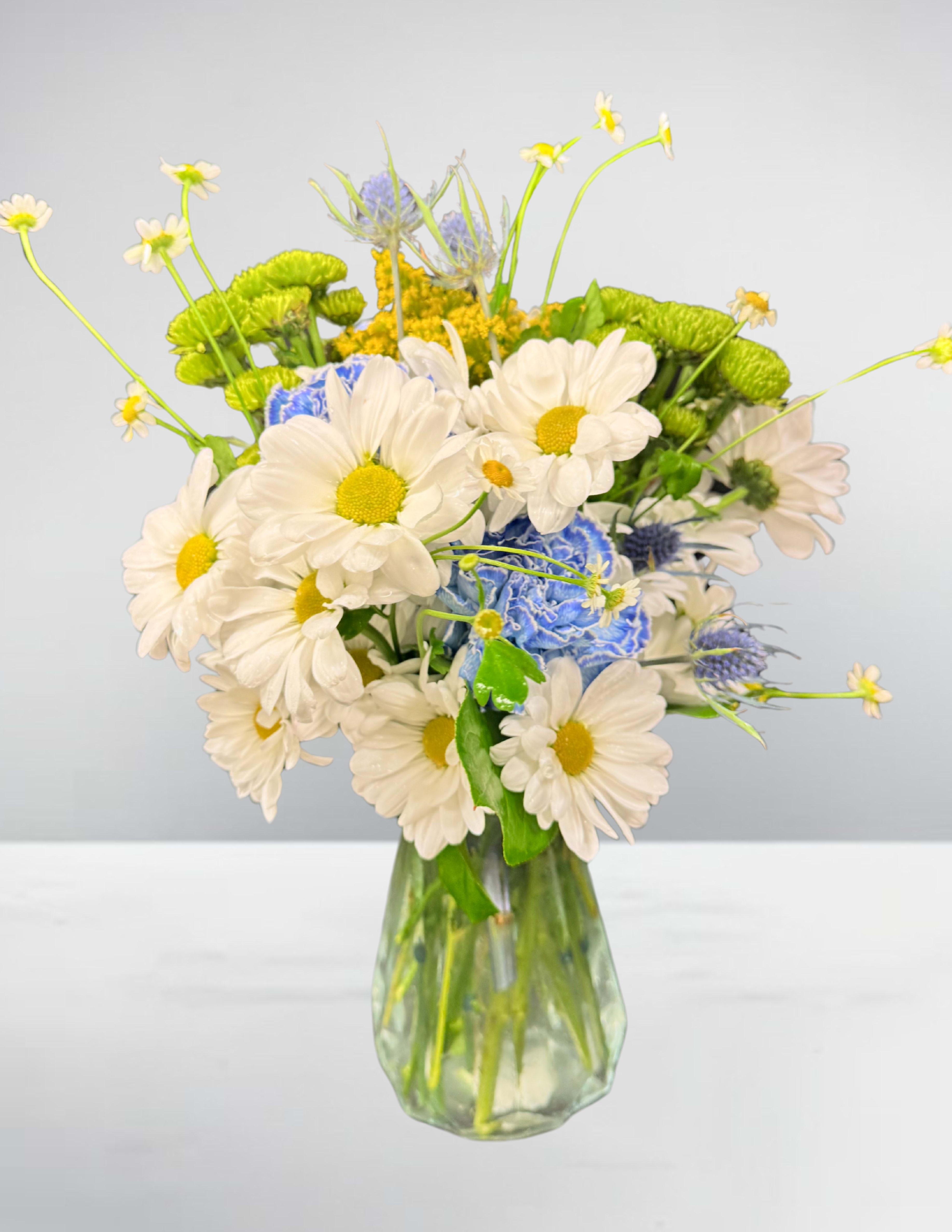 White daisies and blue flowers in a clear glass vase