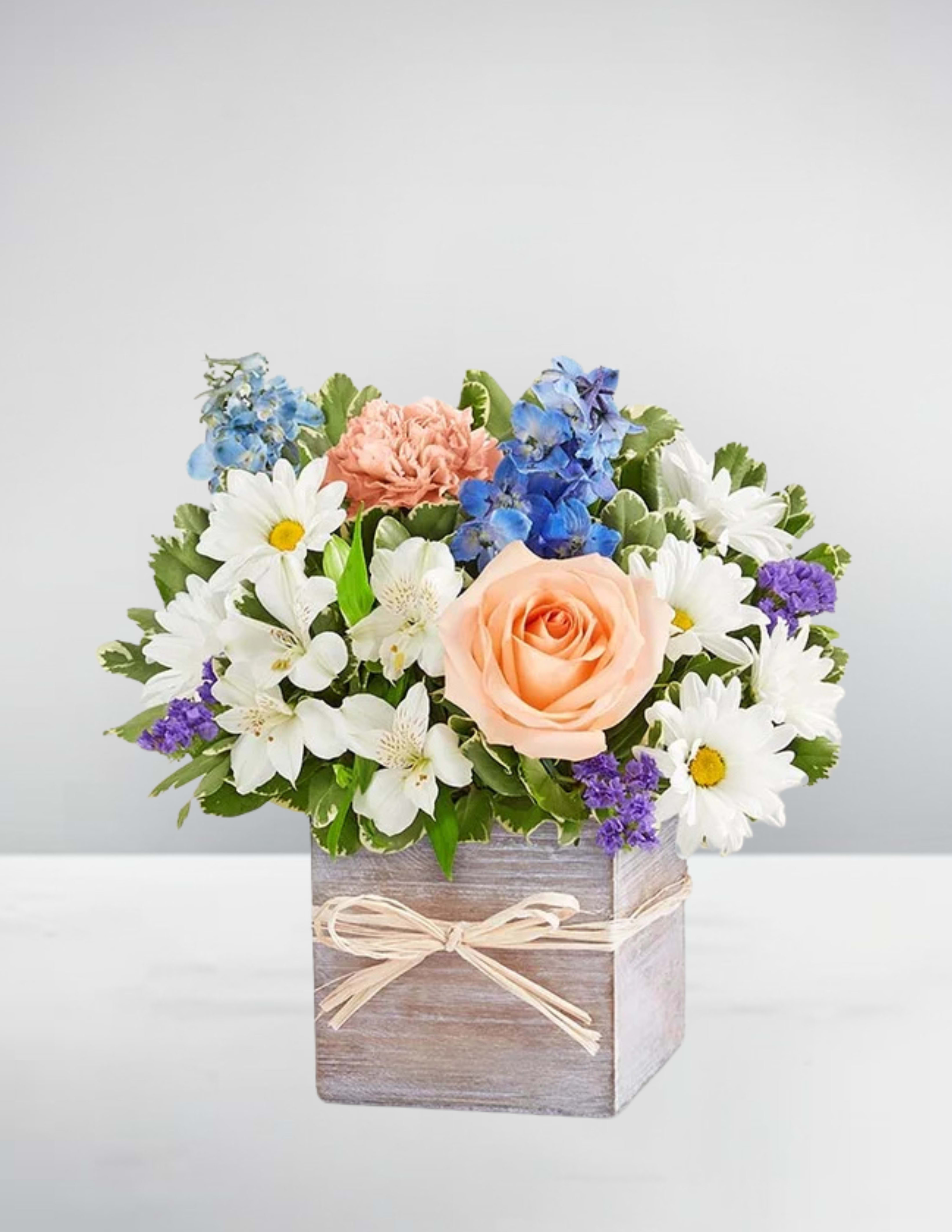 Mixed bouquet with a peach rose, white daisies, and blue flowers in a wooden box