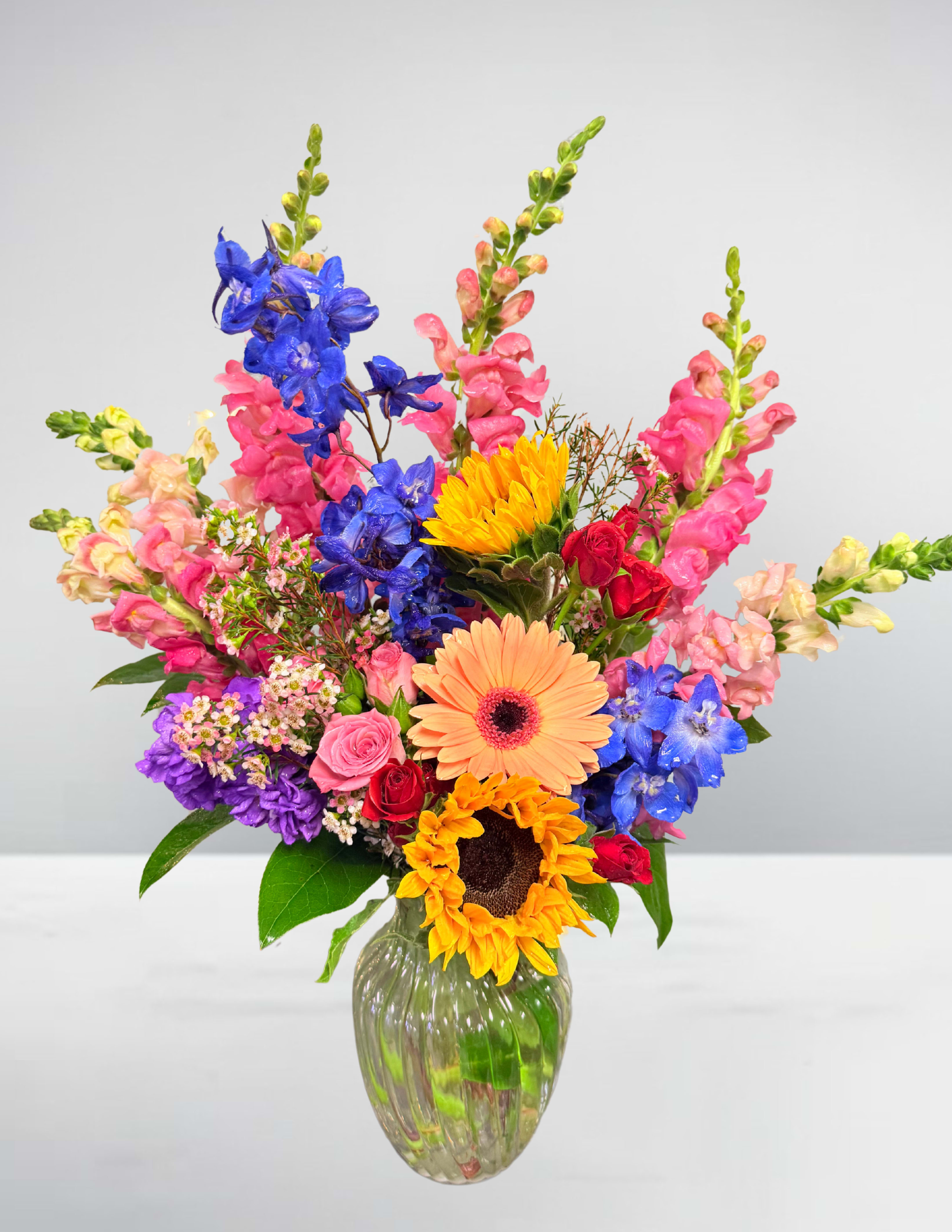 Colorful mixed bouquet in a clear glass vase with sunflowers and gerbera daisies