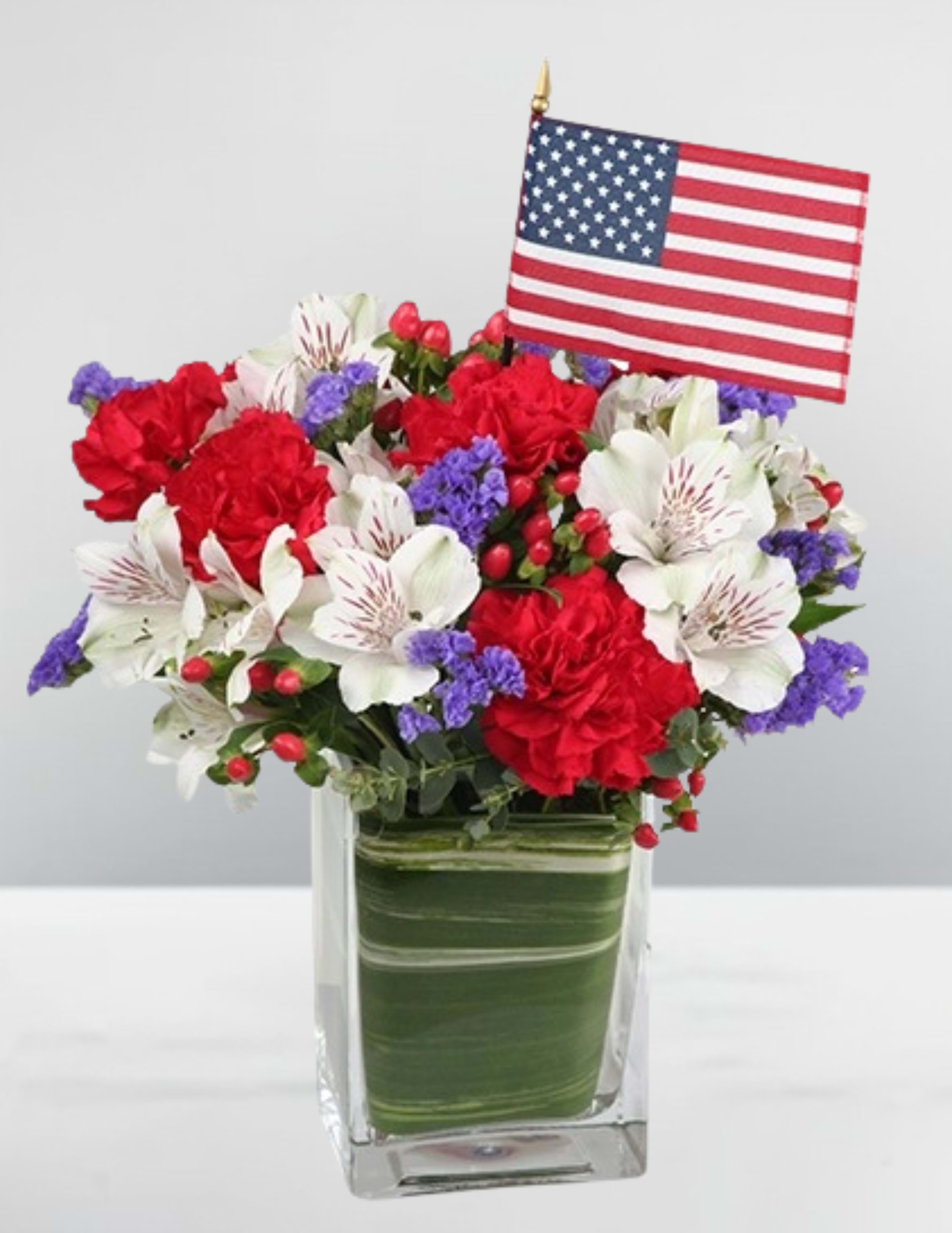 Red, white, and purple floral arrangement in a glass vase with an American flag