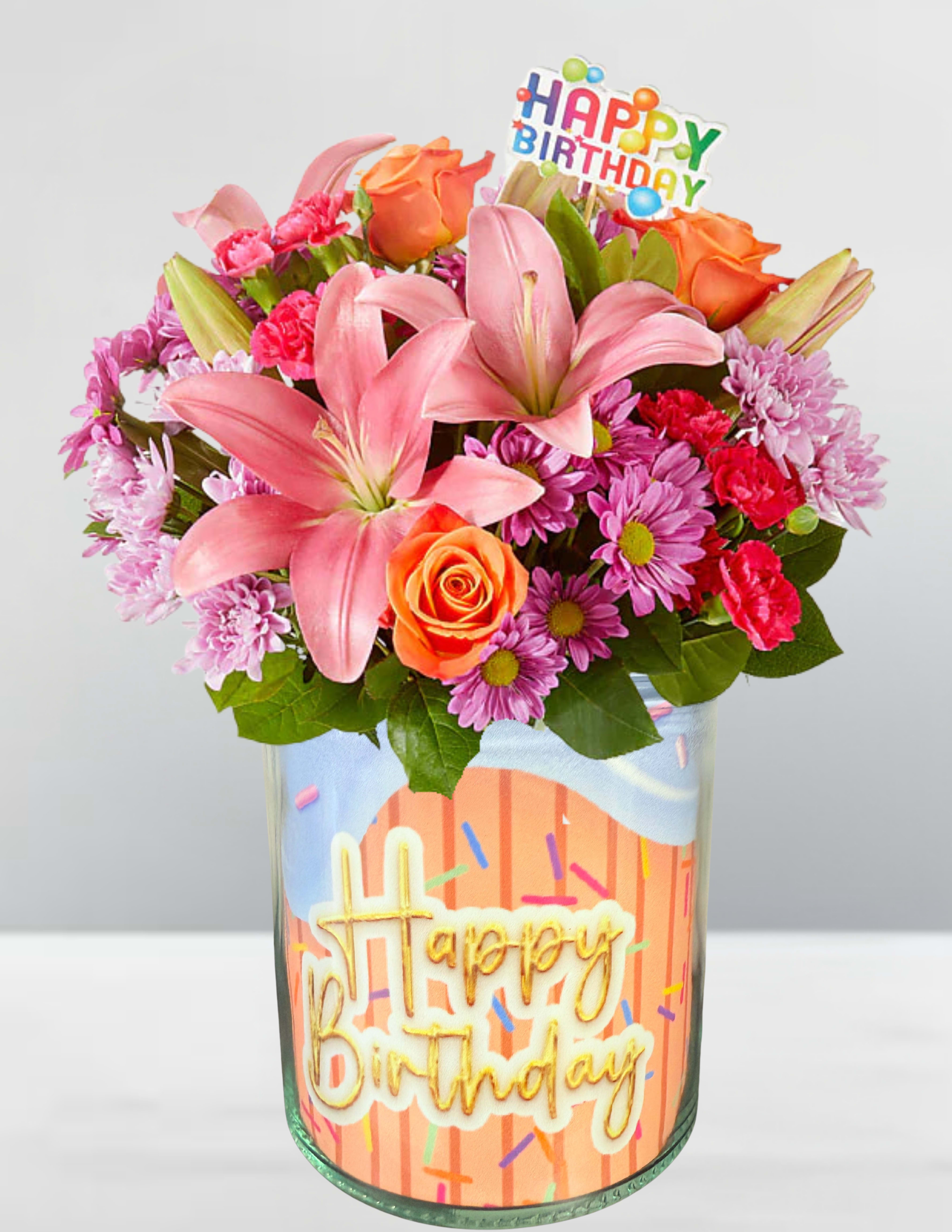 Birthday bouquet with pink lilies, orange roses, and purple daisies in a glass vase