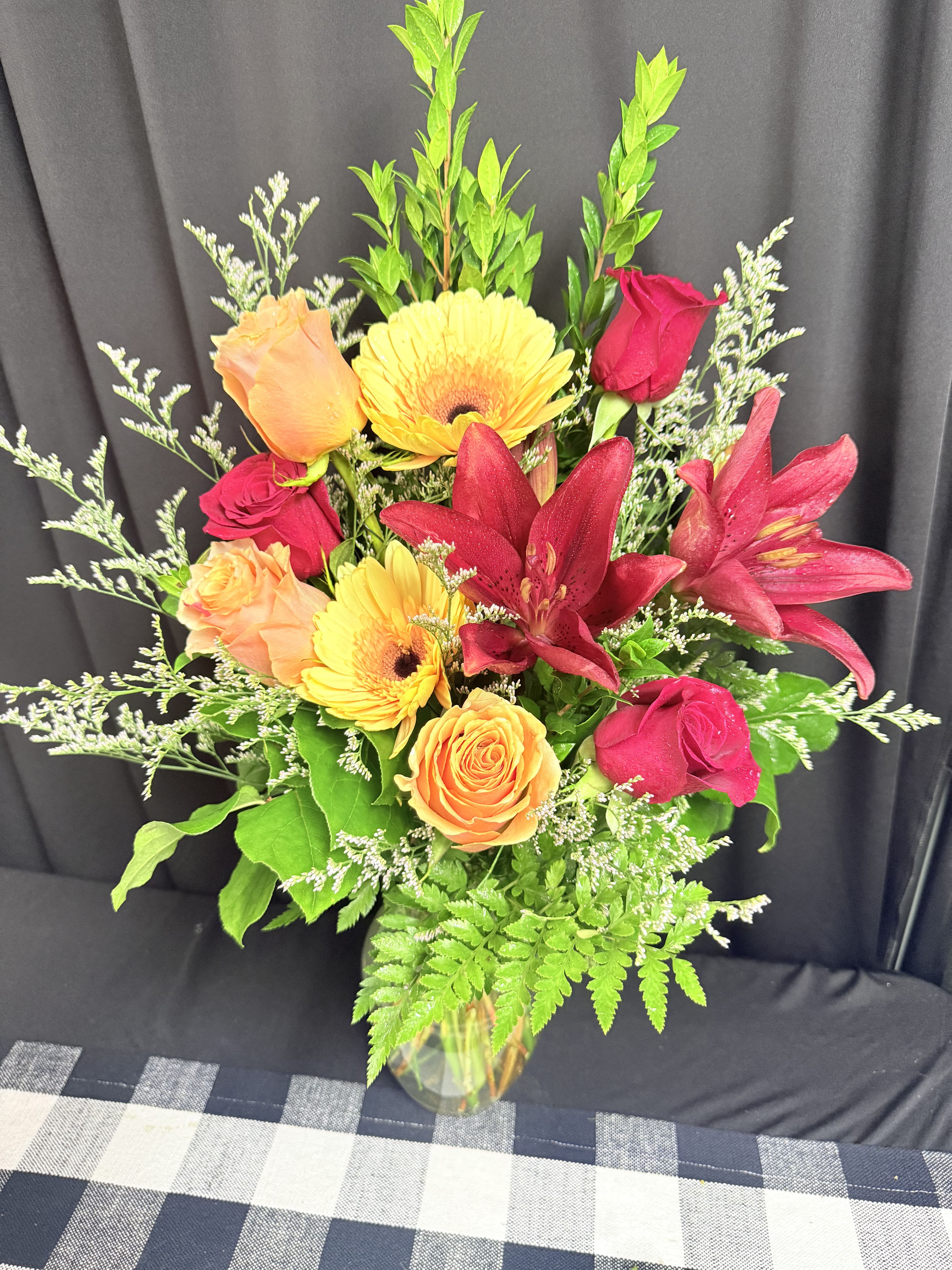 Mixed bouquet of roses, gerbera daisies, and lilies in a glass vase