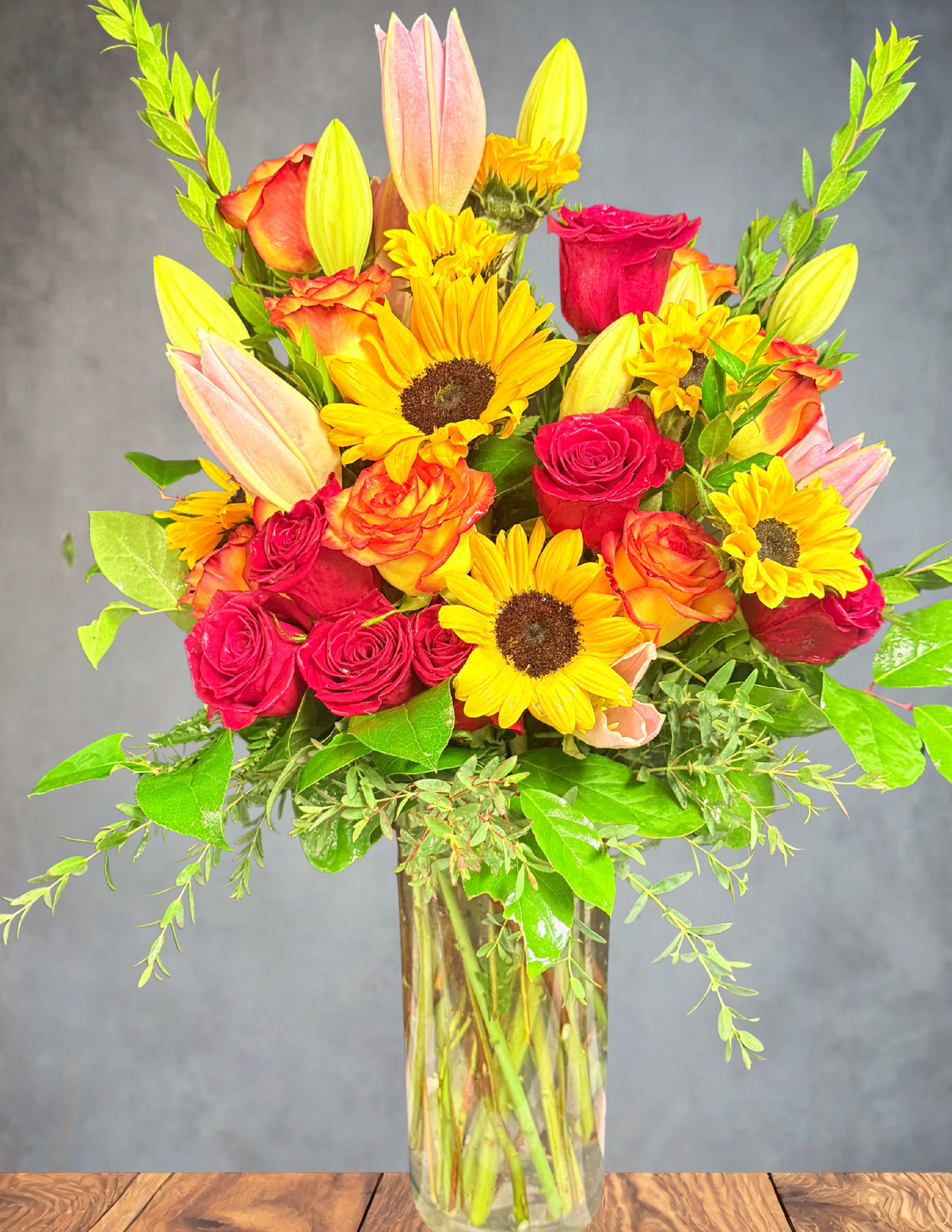 Mixed bouquet of roses, sunflowers, and lilies in a glass vase