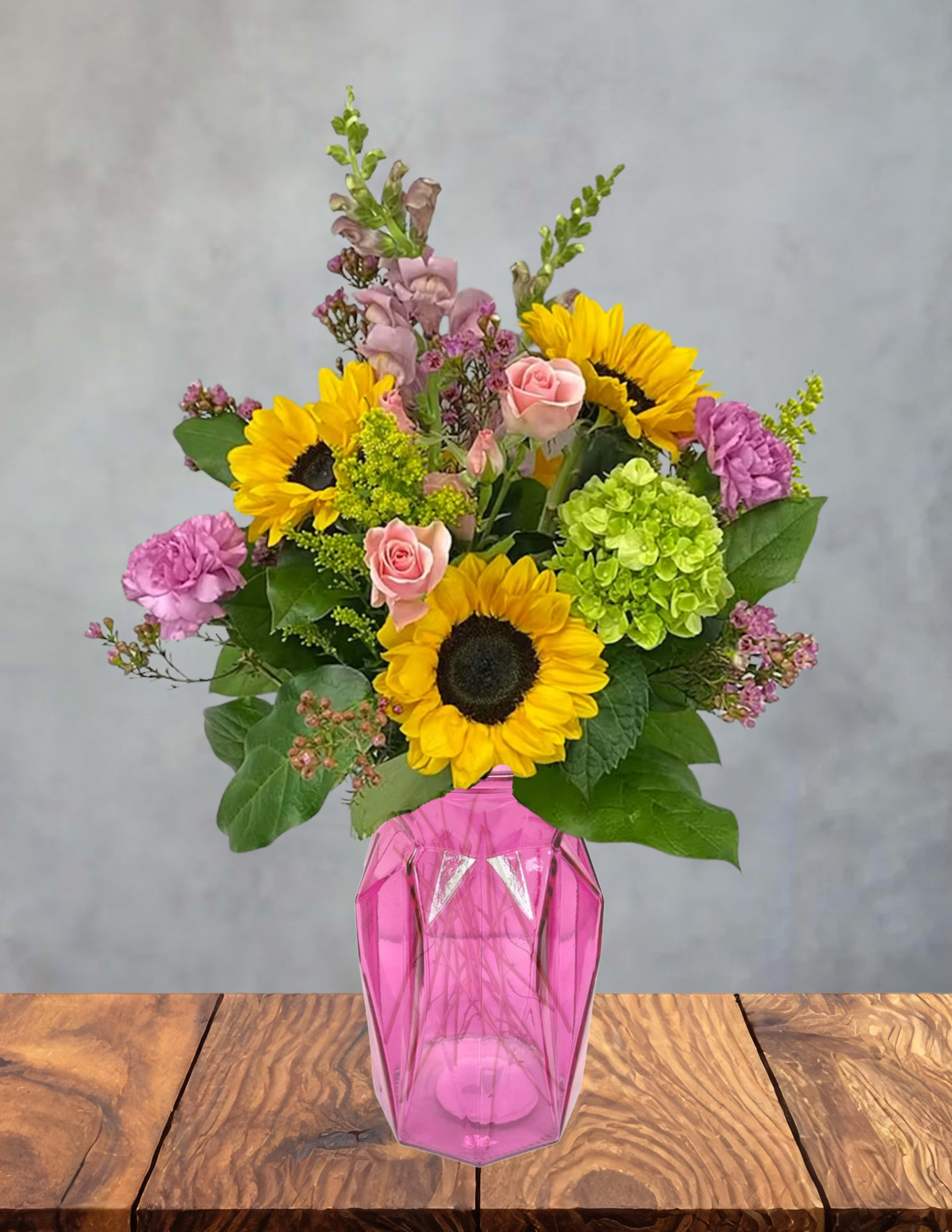 Bouquet of sunflowers, pink roses, and purple flowers in a pink vase
