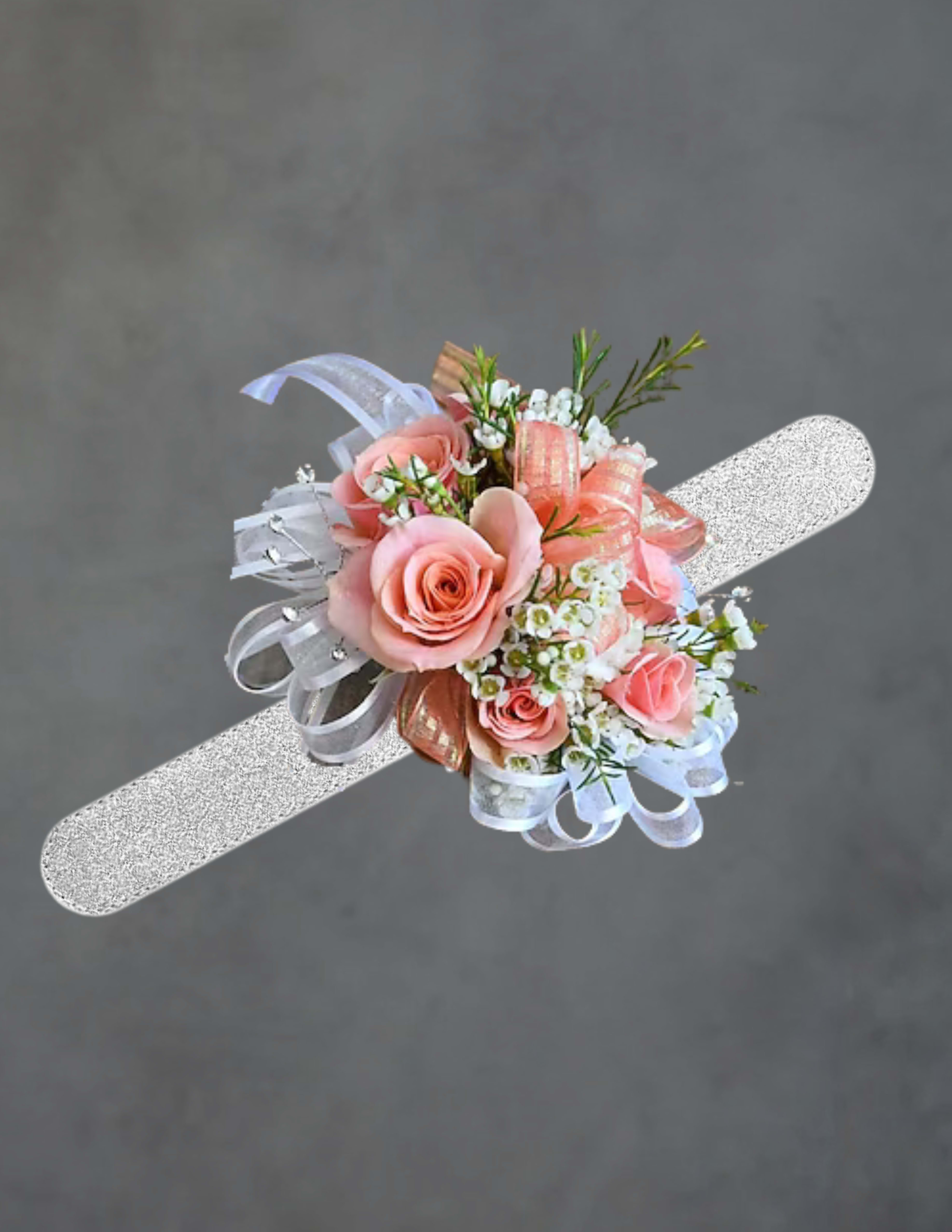 Peach corsage - Soft peac hroses clustered into a compact Peach corsage create an instantly romantic, feminine accent perfect for prom, weddings, or any dressy celebration. The pastel palette of pink and white with delicate filler blossoms and sprigs of greenery gives the person you're thinking of a soft, polished look that reads both classic and photo-ready.  This wrist corsage is mounted on a glittery silver wristband and finished with layered white and pink ribbons for an elegant, formal touch. The arrangement is small and tightly clustered for comfortable wear, combining roses with tiny white filler blooms and green accents to keep the silhouette neat and refined.  Choose this corsage to make a loved one feel celebrated on graduation, bridal events, or a special evening-it's the kind of floral accessory that completes a dress and draws warm compliments. Care: keep it cool and mist lightly; arrive at the venue a little early so the corsage can be secured and adjusted for comfort.
