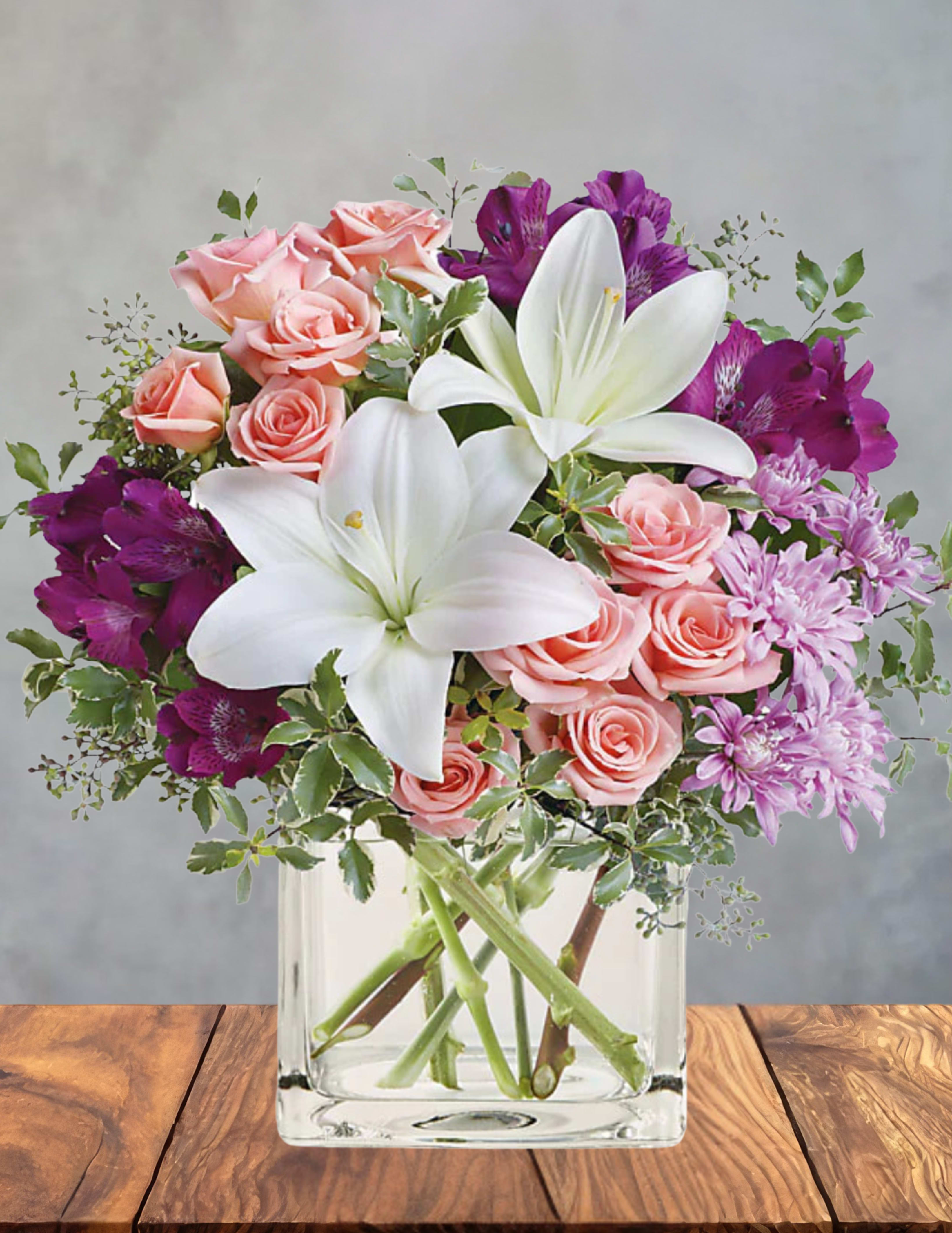 Pastel dream - Soft pink roses and large white lilies mingle with vivid purple alstroemeria in a clear glass vase to create a Pastel dream that feels both romantic and lively-a perfect birthday bouquet or anniversary arrangement that will make the person you're thinking of feel truly celebrated. The rounded, tightly clustered design sits above a rectangular clear glass vase for a classic, everyday presentation that reads thoughtful and elegant whether you're saying "thank you," sending a just-because surprise, or honoring Mom on Mother's Day.  This arrangement includes alstroemeria, chrysanthemums, daisies, lilies, and roses in a palette of pinks, purples, whites, and fresh greens, layered for depth and texture so each bloom is visible from every angle. The clear glass vase keeps the focus on the flowers' soft petals and lively hues; the overall size is full and substantial without being oversized, fitting comfortably on a dining table, desk, or bedside table. Delivered ready to display, it's an easy, meaningful way to make someone feel truly seen and appreciated-ideal for birthdays, anniversaries, thank-you gestures, or simply brightening an ordinary day.
