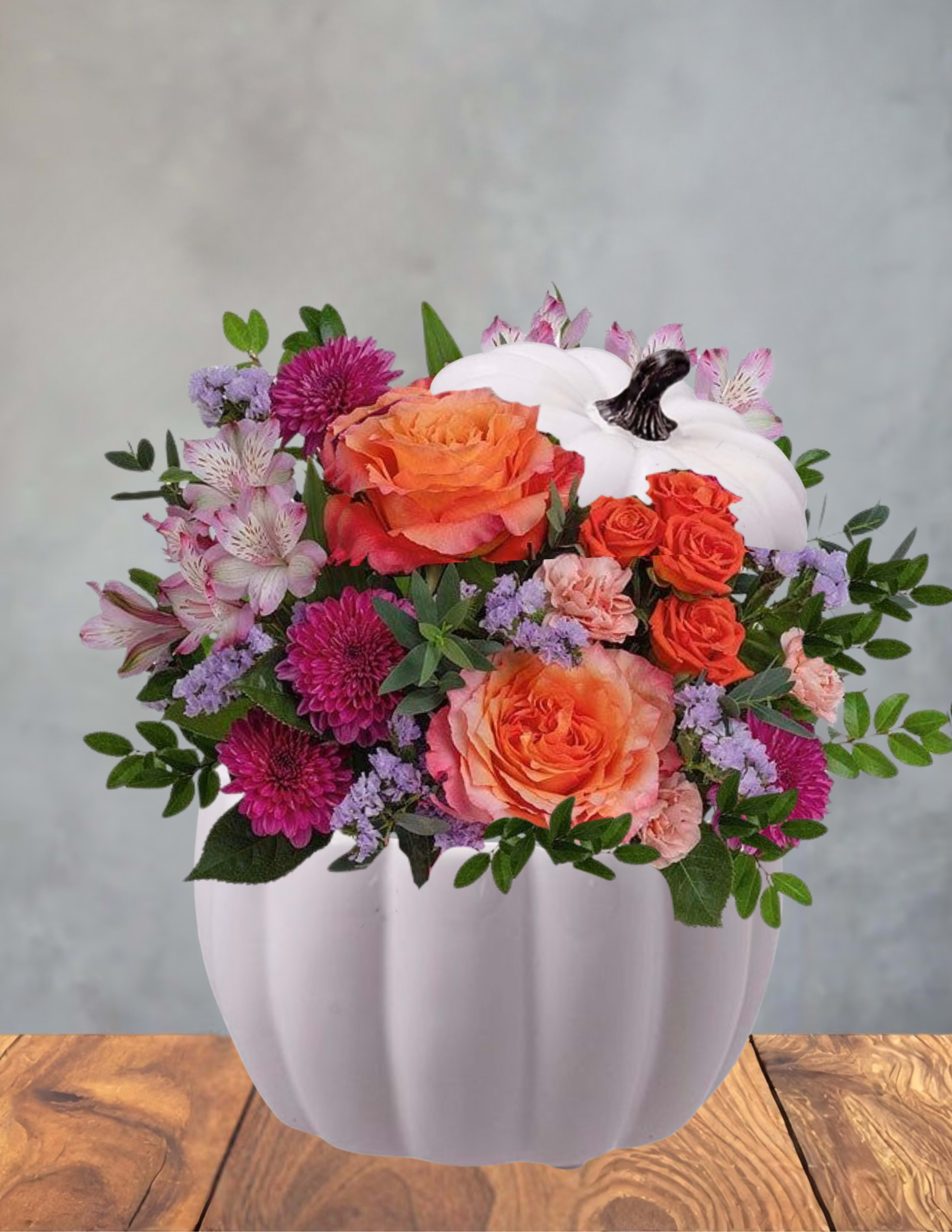 Fireside pumpkin - A cheerful autumn centerpiece that feels both cozy and playful, this fall flower arrangement in a white pumpkin-shaped vase is perfect as a Thanksgiving centerpiece or a seasonal gift. The Fireside pumpkin arrangement is built as a rounded bouquet-style display - the kind of piece that makes the person you're thinking of smile when they walk into the room and catch that burst of warm color on the table.  Dense clusters of orange roses, pink carnations, and purple chrysanthemums are balanced with pale alstroemeria and fresh greenery for contrast; daisies and soft white accents lift the palette and keep the composition bright. The white pumpkin-shaped vessel adds a festive, handcrafted touch that reads seasonal without leaning too rustic, while the compact, full shape gives a polished look ideal for tabletops, mantels, or entry consoles.  Made to mark fall moments - Thanksgiving dinners, hostess gifts, or a cozy birthday in autumn - this arrangement arrives ready to display and brings an immediate feeling of warmth and celebration to the recipient. Standard care: keep flowers in fresh water and away from direct heat to extend vase life.