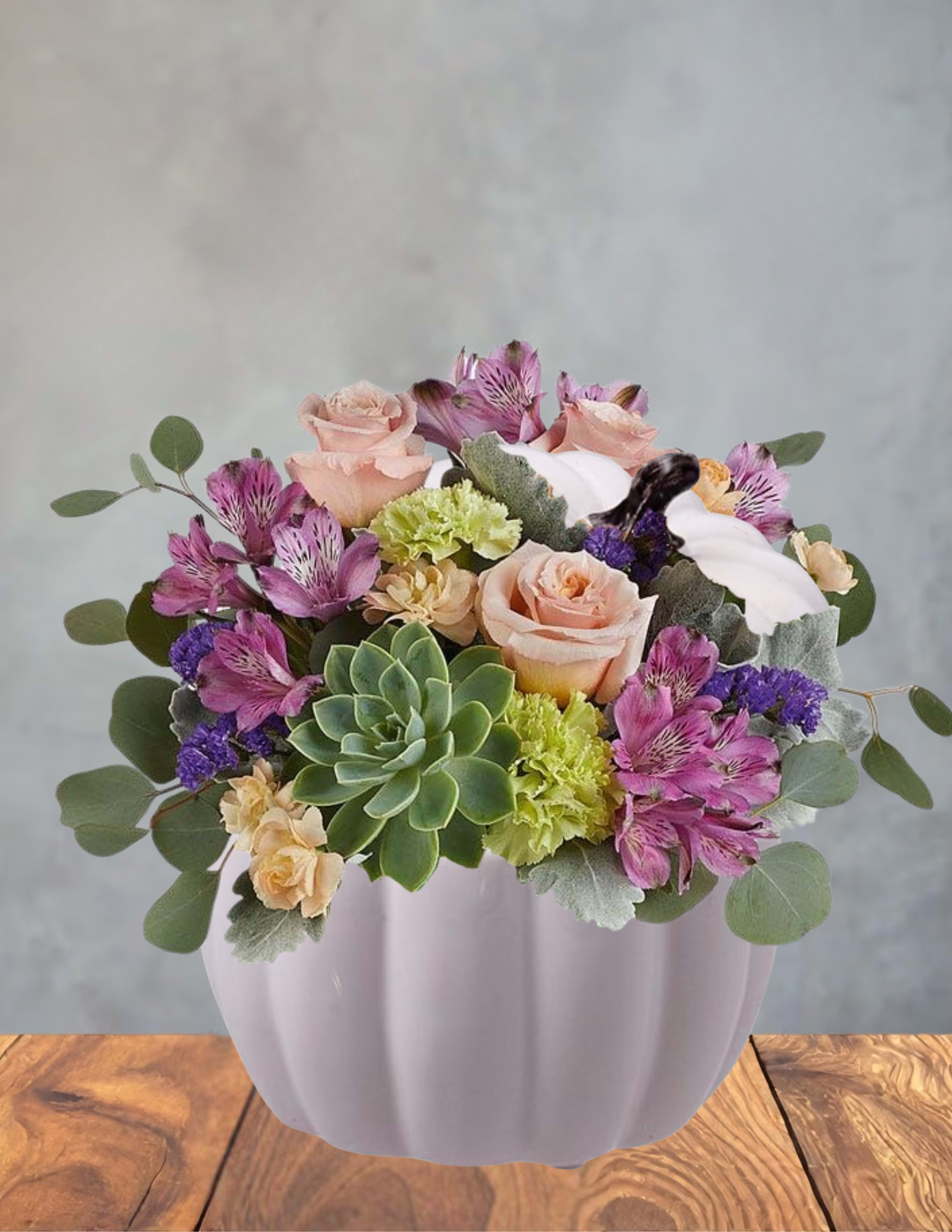 Blush &amp; Sage Harvest - A soft blend of blush roses and lavender alstroemeria makes an immediate romantic impression in this low, garden-style flower arrangement for anniversaries, spring celebrations, or simply to make someone feel cherished. The rounded white ceramic vase and a large central succulent give the design a modern touch while keeping the overall mood warm and decorative-perfect for the person you're thinking of who loves both classic blooms and contemporary texture.  This arrangement features blush roses, purple alstroemeria, pale green carnations, and a prominent succulent at the center, arranged full and low so blooms spread outward for a lush, abundant look. The palette of pink, purple, green, and white reads soft and fresh; the white ceramic vase complements the pastel tones and keeps the focus on the layered petals and contrasting succulent form.  Choose this piece when you want to celebrate a milestone or brighten someone's day with a versatile, elegant gift-the kind of bouquet that makes the recipient feel seen and celebrated. The compact, outward-spreading composition works well on a dining table, desk, or bedside table; care is simple-keep water fresh and in a cool spot away from direct sun to extend the life of the blooms and succulent.