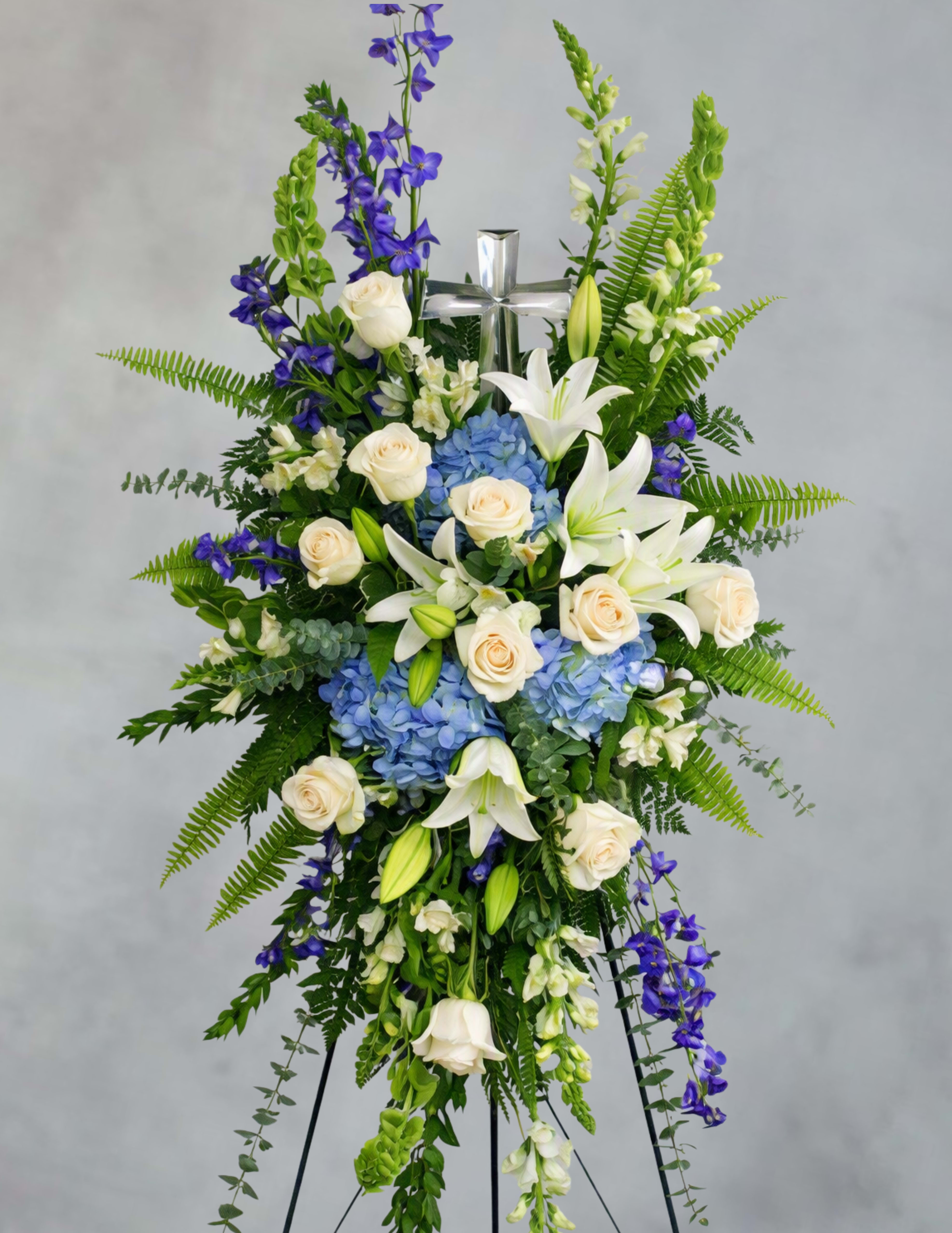 Standing floral spray with white lilies, cream roses, blue hydrangeas, and purple flowers