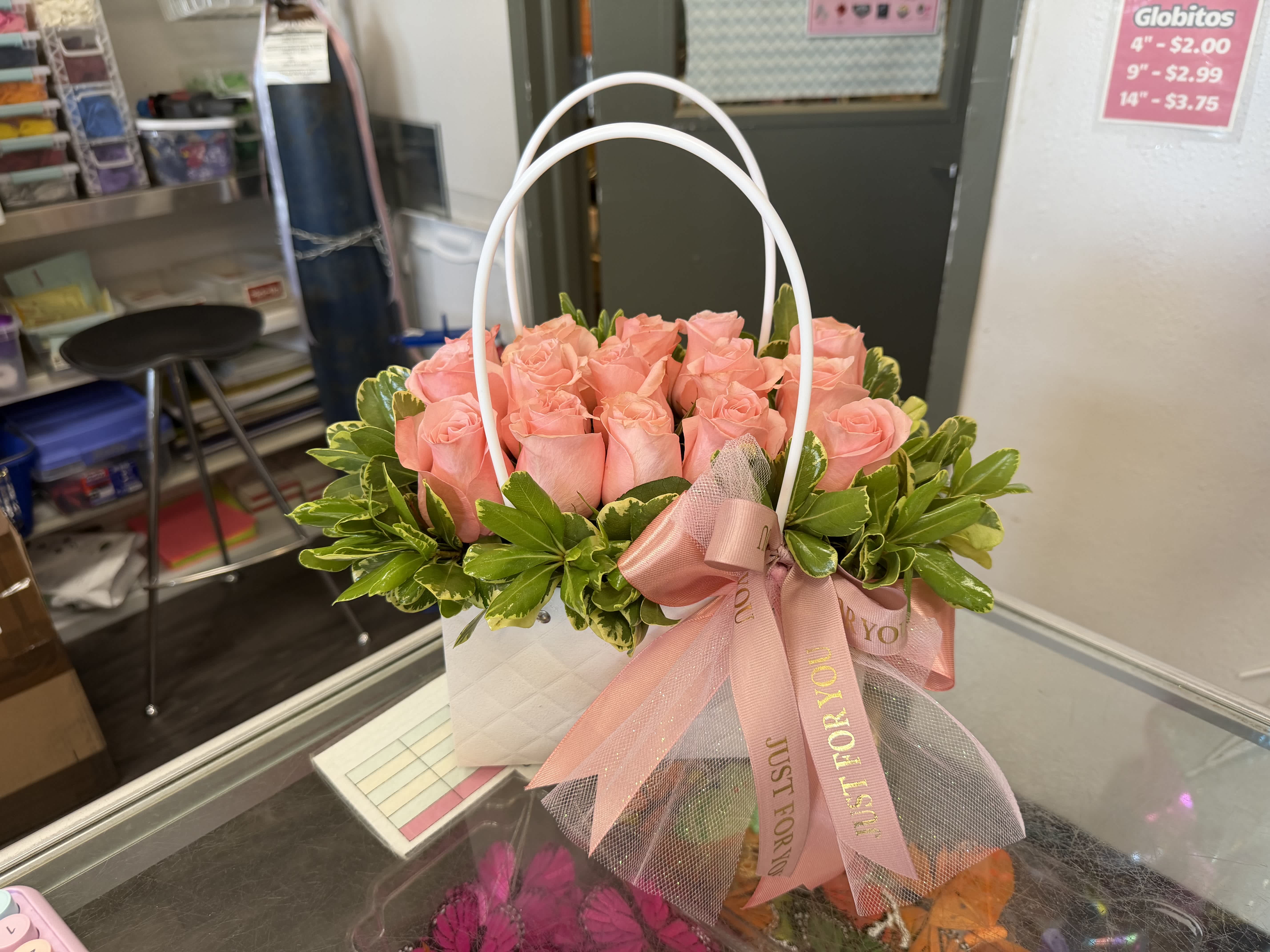 Pink roses arranged in a white handled gift basket with a pink ribbon
