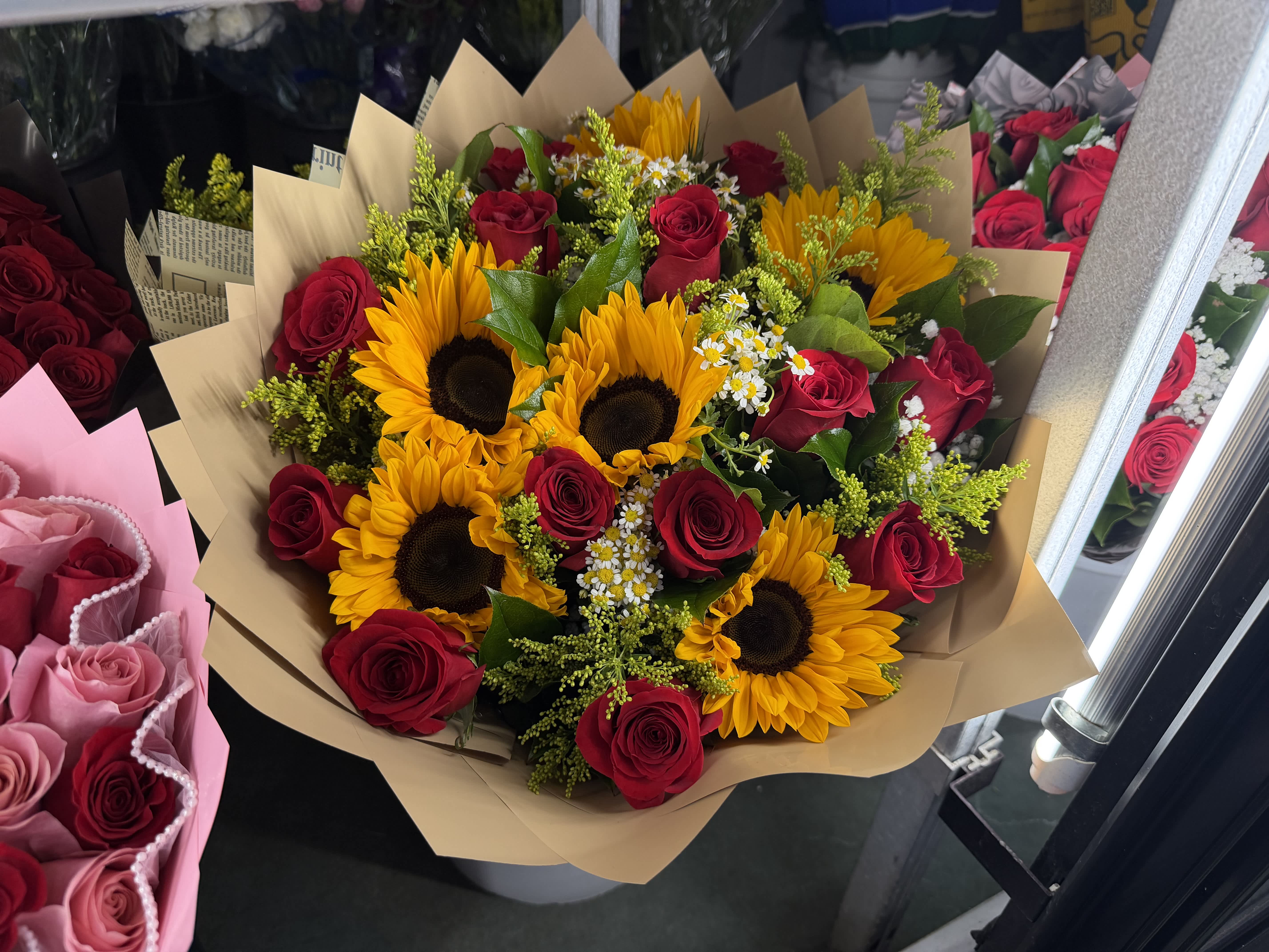 Bouquet of red roses and yellow sunflowers wrapped in tan paper