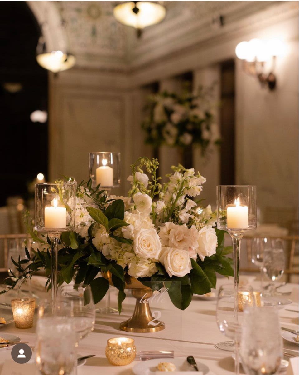 Low &amp; Lush Wedding Centerpiece - A low, classic wedding centerpiece designed to feel timeless, romantic, and guest-friendly (no tall arrangements blocking the table). Expect a lush mix of white/ivory blooms with fresh greenery, arranged in a clean, elegant style, perfect for candlelit receptions, traditional weddings, and modern minimal vibes.  Perfect for: guest tables, sweetheart table accents, head table clusters Style: low + full, soft and airy, classic white/green palette Flowers: seasonal mix (ex: roses, hydrangea, spray roses, ranunculus, lisianthus + premium greens) Color options: white/ivory (can be customized to your palette)  Good to know:  Vessels may vary slightly based on availability (compote/low bowl style), but the look stays consistent.  Seasonal substitutions may happen—we keep the same color story + overall vibe.  Candles/candleholders are not included unless added as an upgrade.