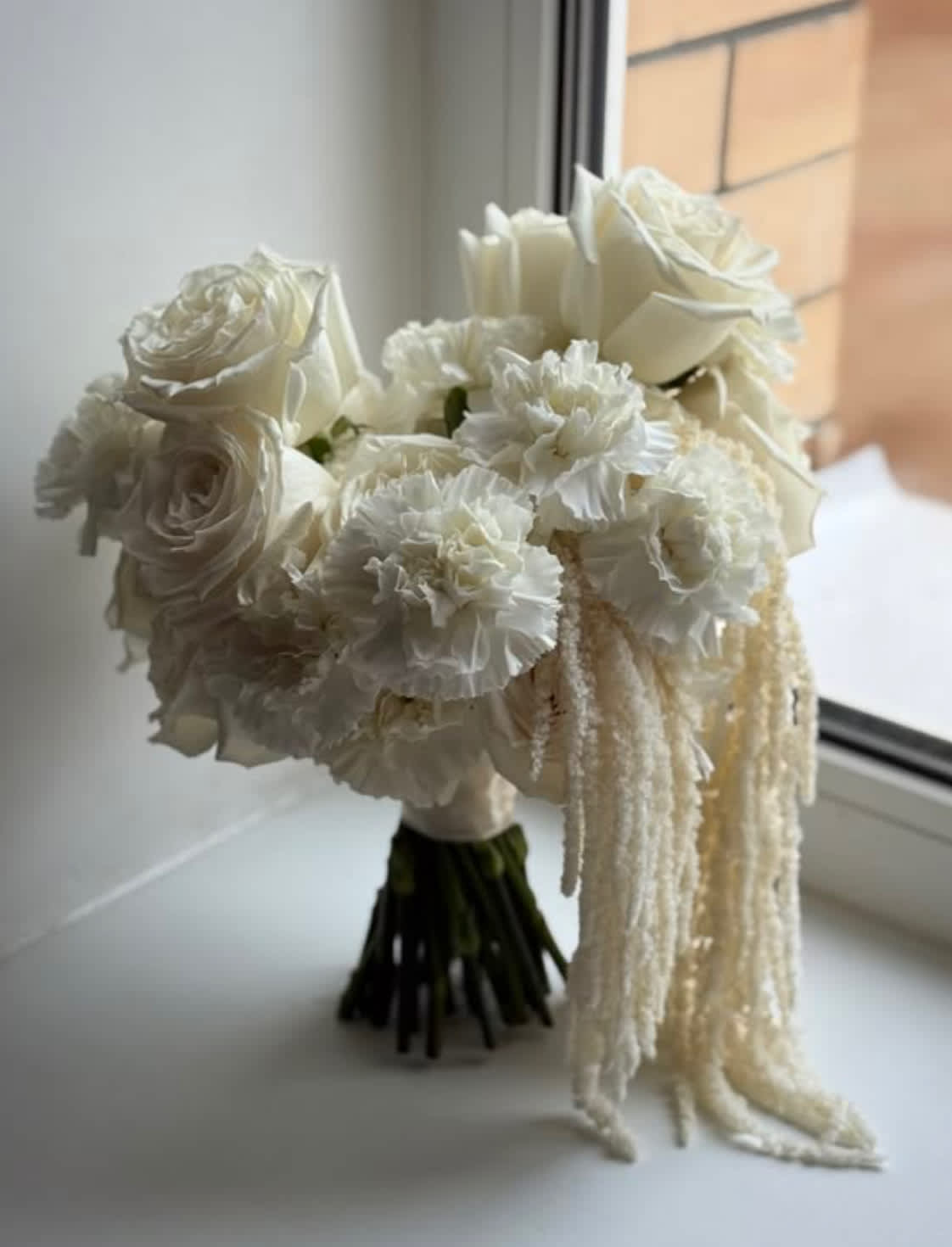 White bridal bouquet with roses and ruffled blooms, finished with trailing strands