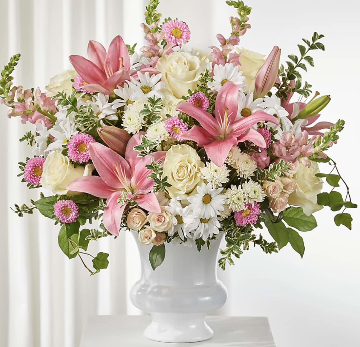 Forever in Bloom -  A Tribute of Love, Grace &amp; Cherished Memories - Celebrate a life beautifully lived with Forever in Bloom, an elegant sympathy arrangement designed to offer comfort, hope, and heartfelt remembrance. Featuring graceful pink lilies, white roses, delicate spray roses, cheerful daisies, and seasonal accents.  Artistically arranged in a timeless white keepsake urn, Forever in Bloom brings warmth and serenity to funeral services, memorial celebrations, or the home of a loved one. Each arrangement is handcrafted by the floral designers at Bloom Luxury Box using the freshest premium blooms available, ensuring every tribute is as unique and meaningful as the life it honors.  Approximate Dimensions: 28"H x 24"W