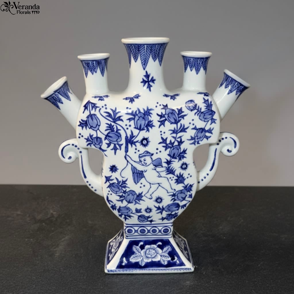 Blue and White Tulipiere (with flowers) - Elevate your floral design with this elegant Blue and White Tulipiere. Inspired by classic Delftware, this vessel features a central spout and four individual side ports, allowing for effortless, structural arrangements. Whether featuring delicate spring bulbs or architectural branches, its unique silhouette makes it a statement piece even when empty. Price includes the vase and designers choice of flowers. 