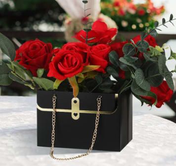 Red roses arranged in a black handbag-style box with gold chain handles.