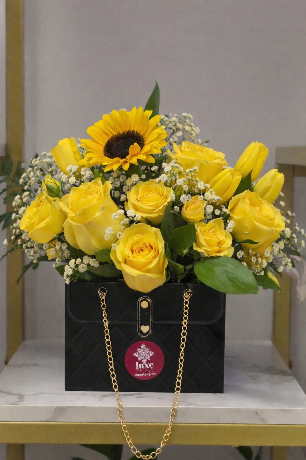 Yellow roses and a sunflower arranged in a black gift box with a gold chain.