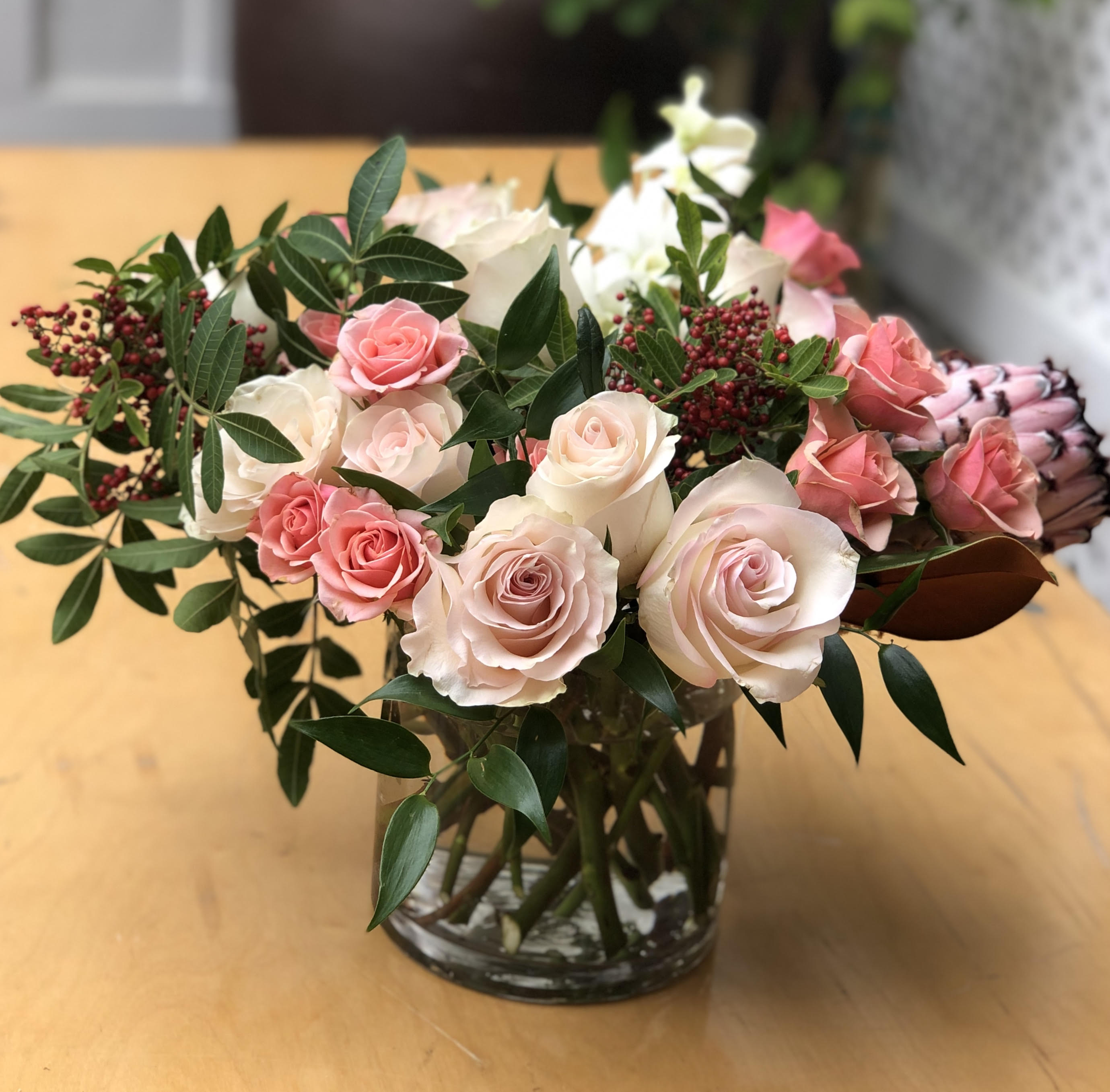 Pink and white roses arranged in a glass vase with greenery