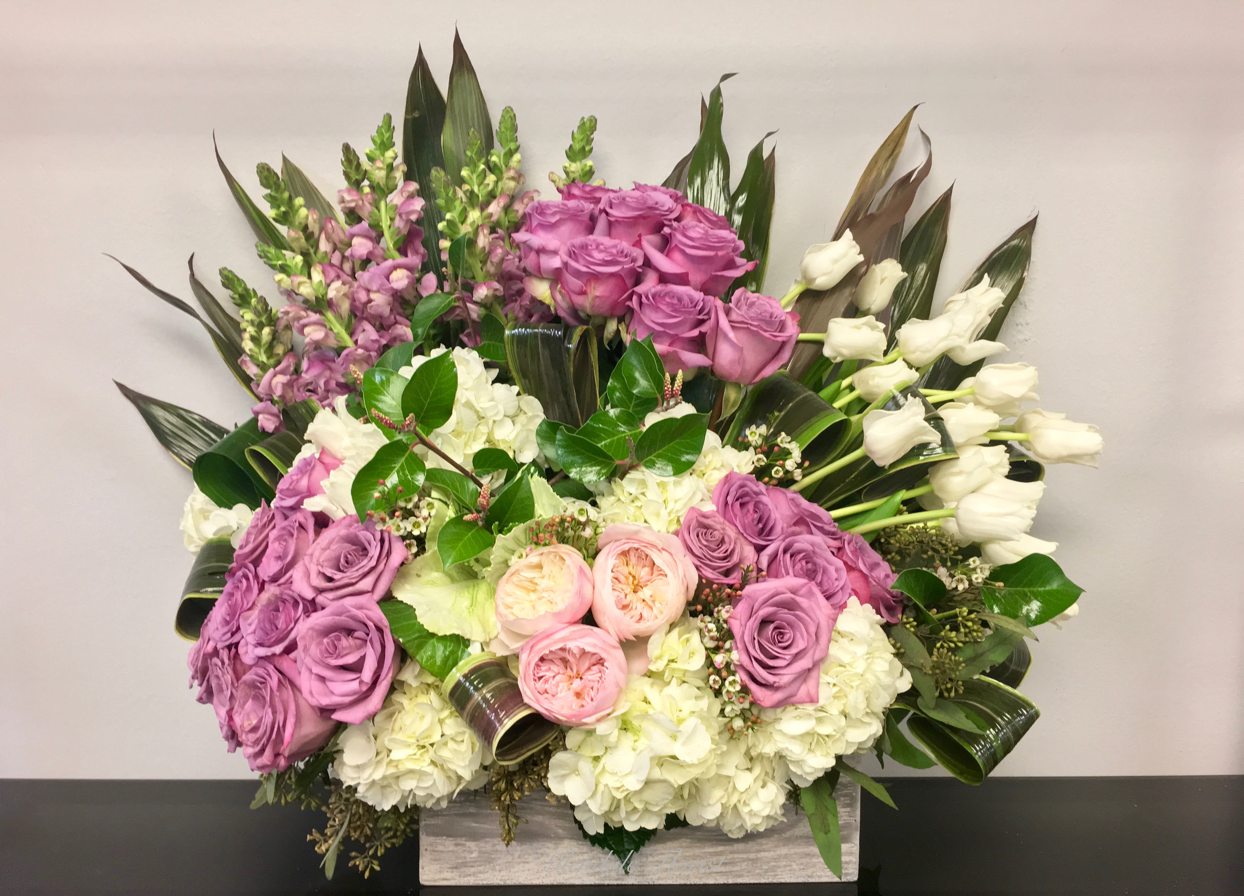 Low rectangular arrangement with lavender roses, white hydrangeas, pink roses, and white tulips.