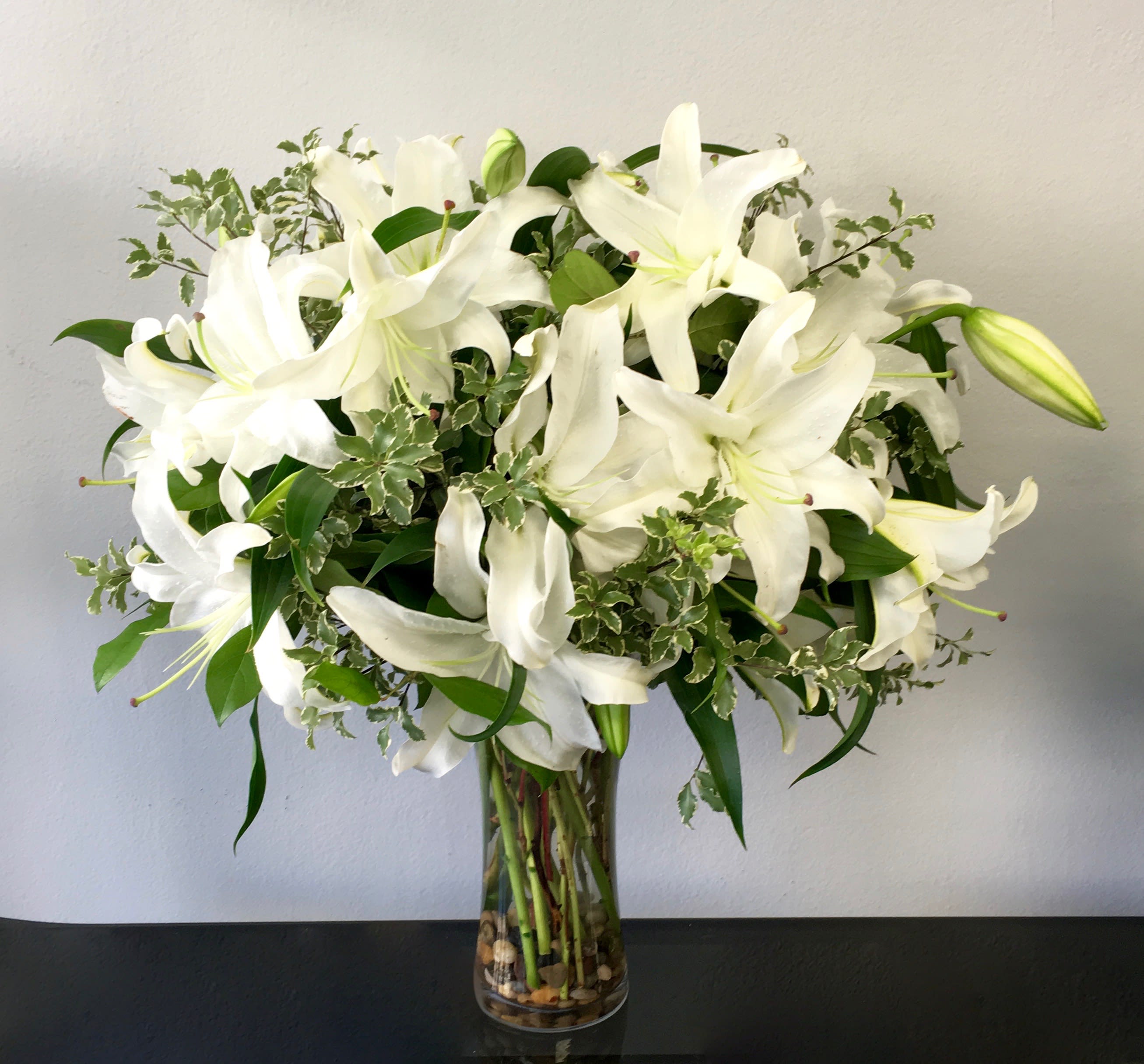 Tall clear vase of white lilies with variegated foliage