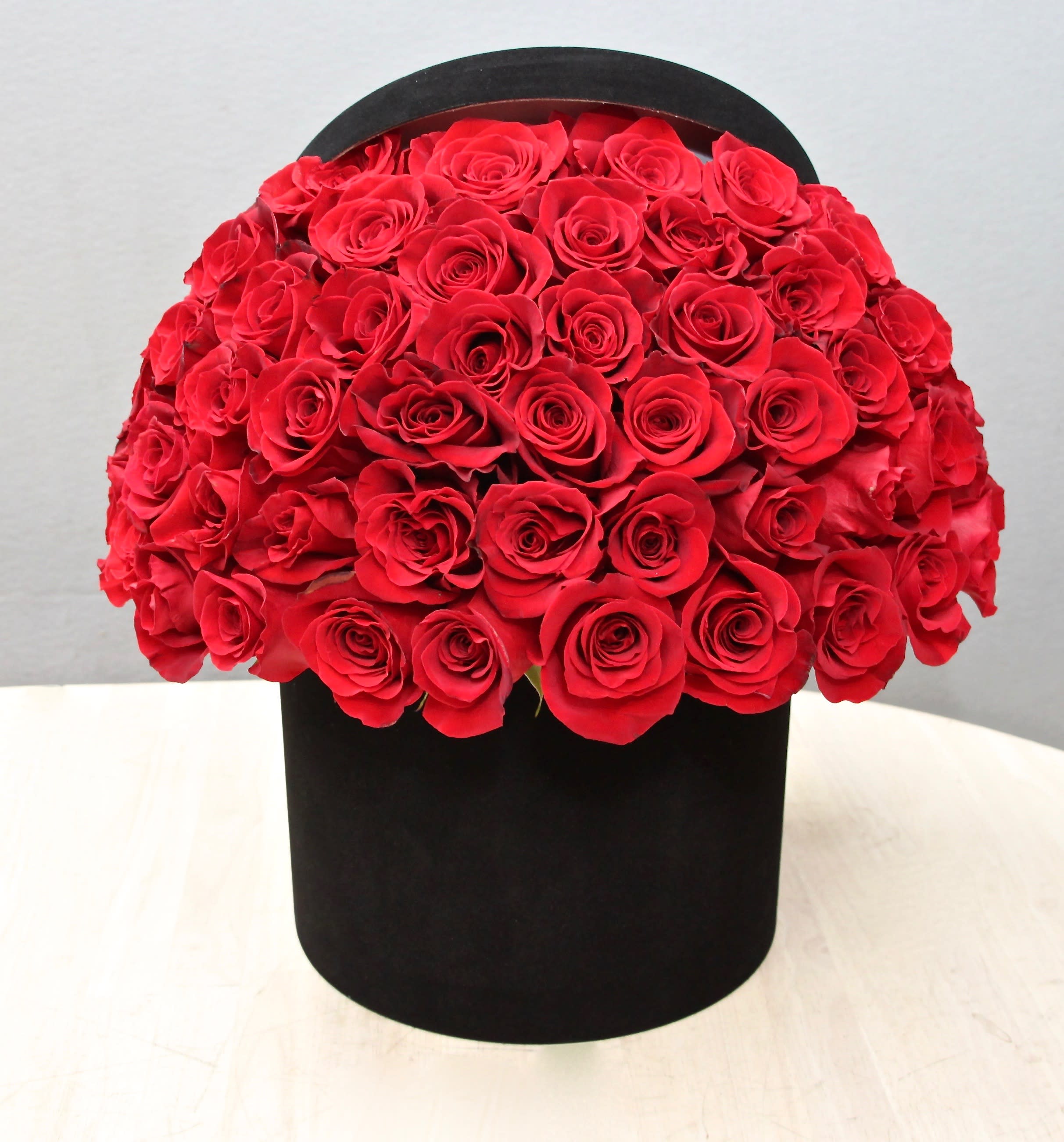 Dome of red roses arranged in a round black hatbox-style container