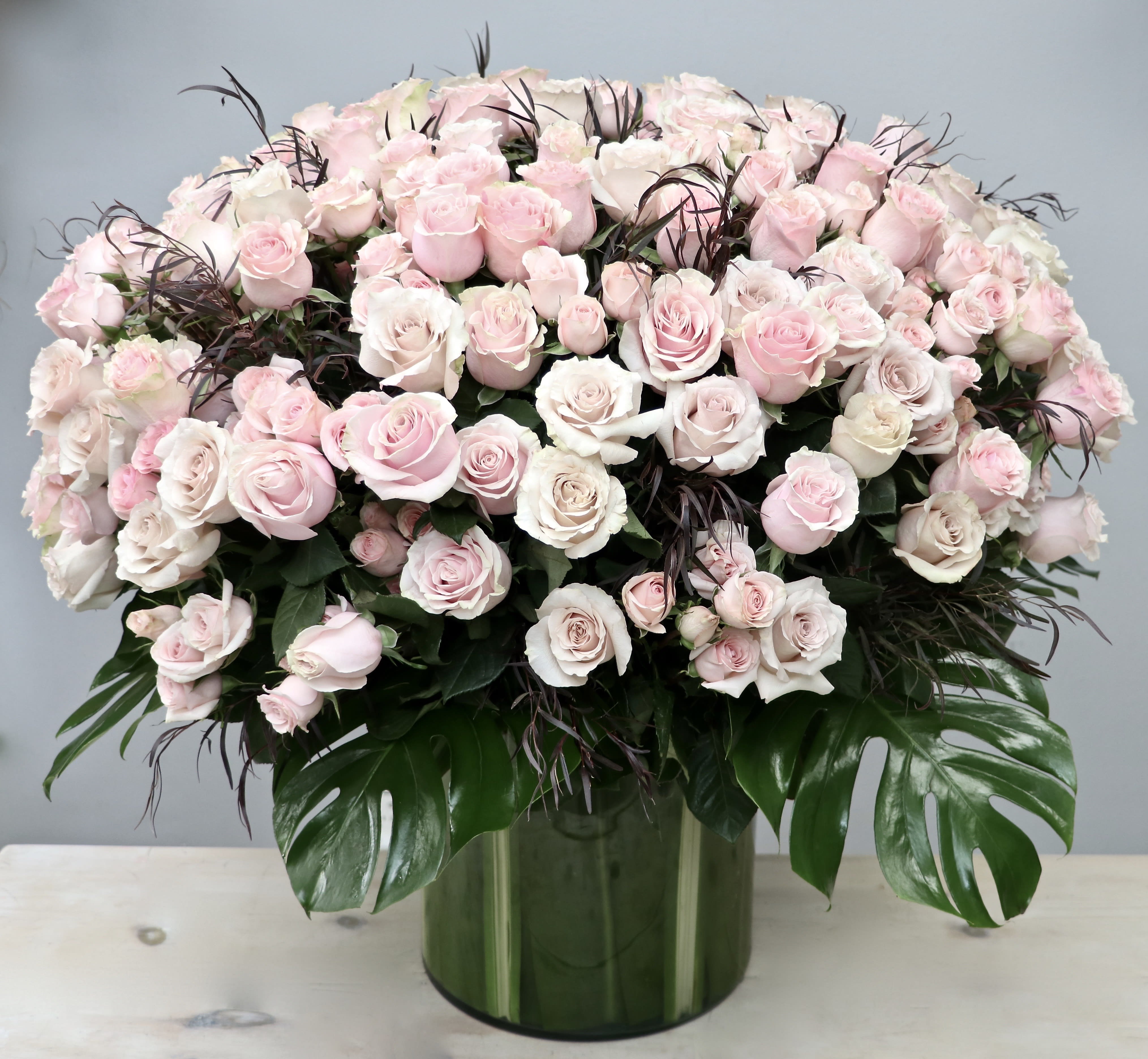 Large dome arrangement of pale pink and white roses in a green glass cylinder vase