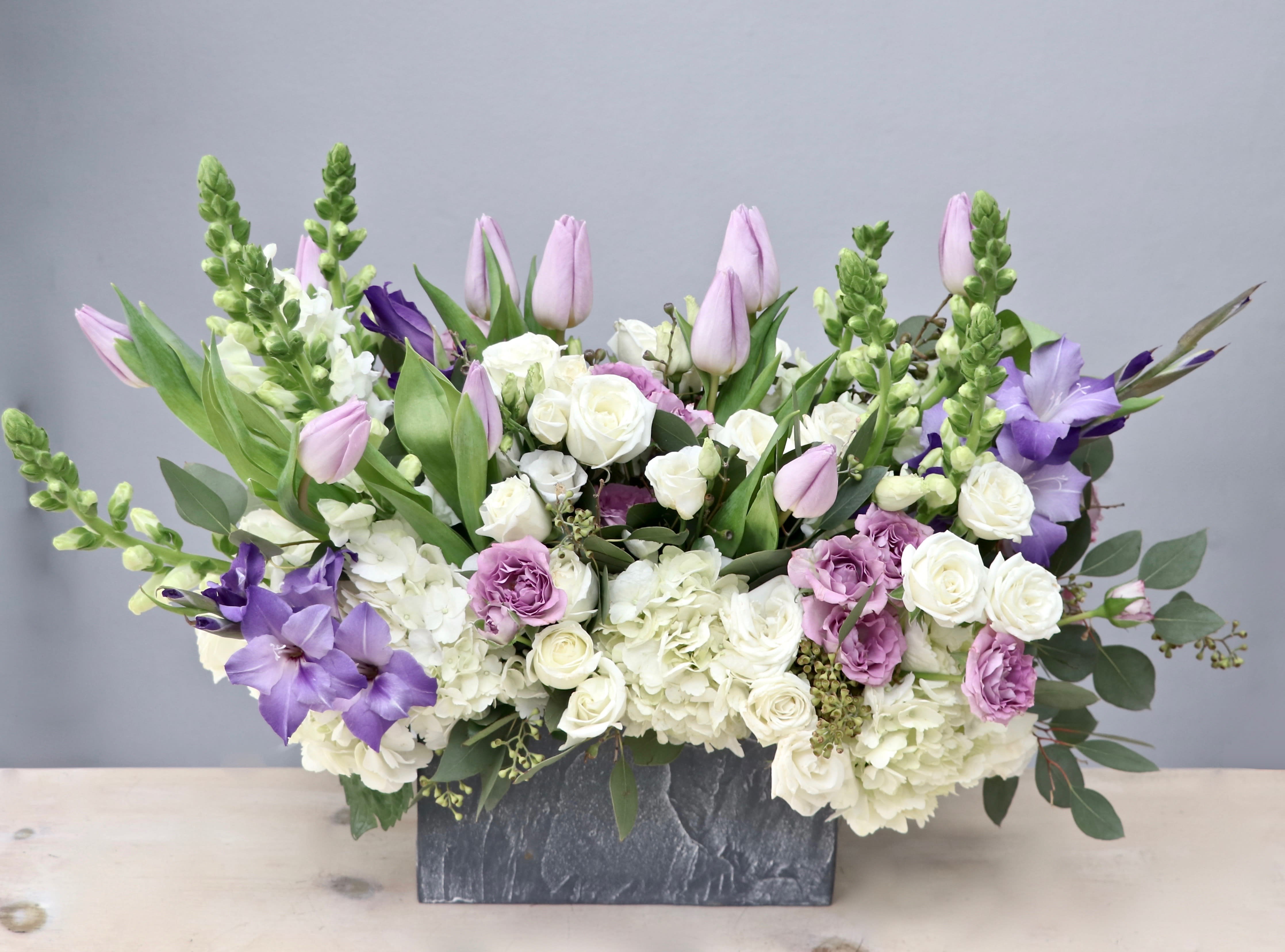 Rectangular arrangement of white and lavender flowers, including tulips and roses, in a gray stone container