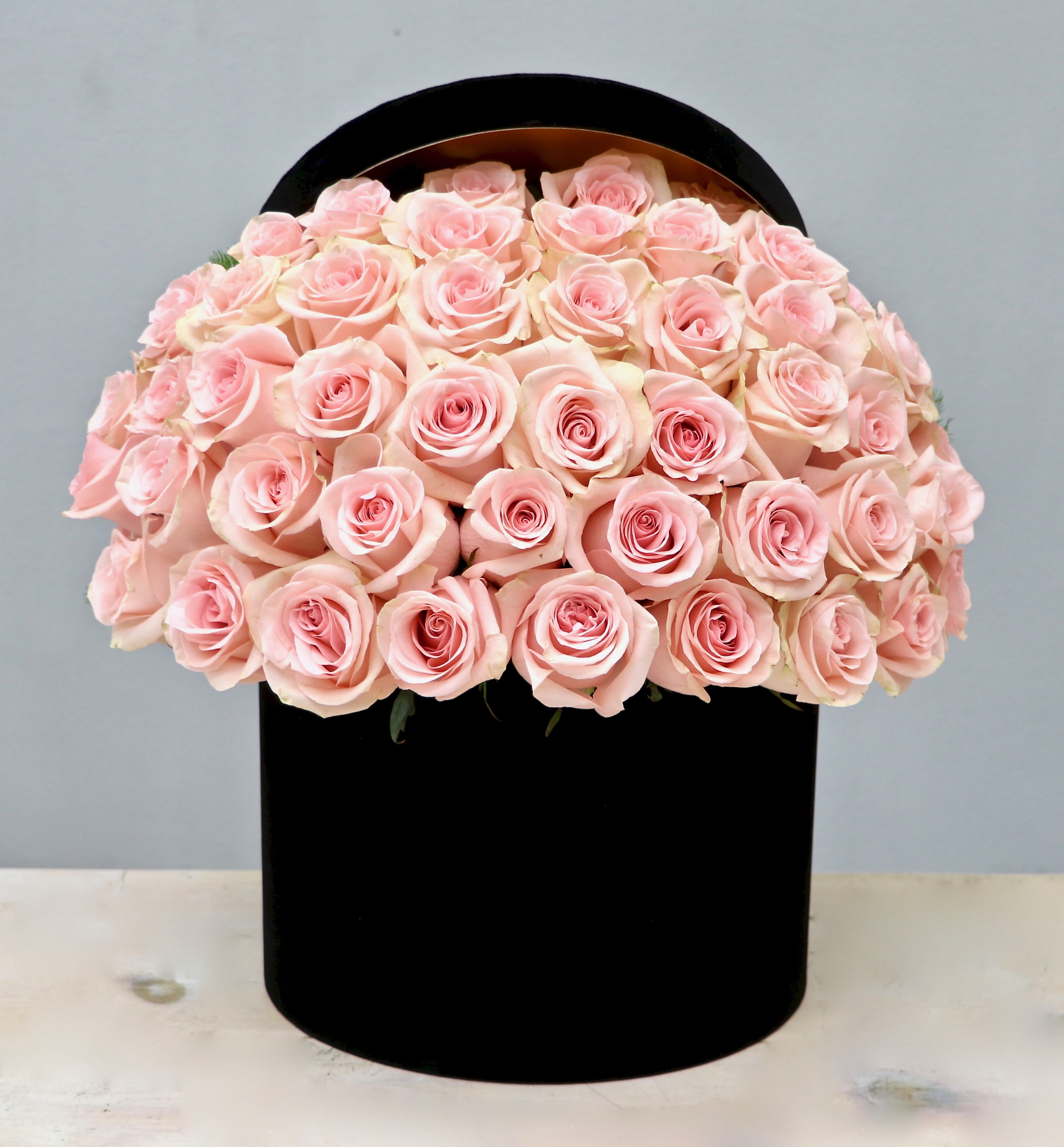 Dome of light pink roses arranged tightly in a round black hatbox-style container