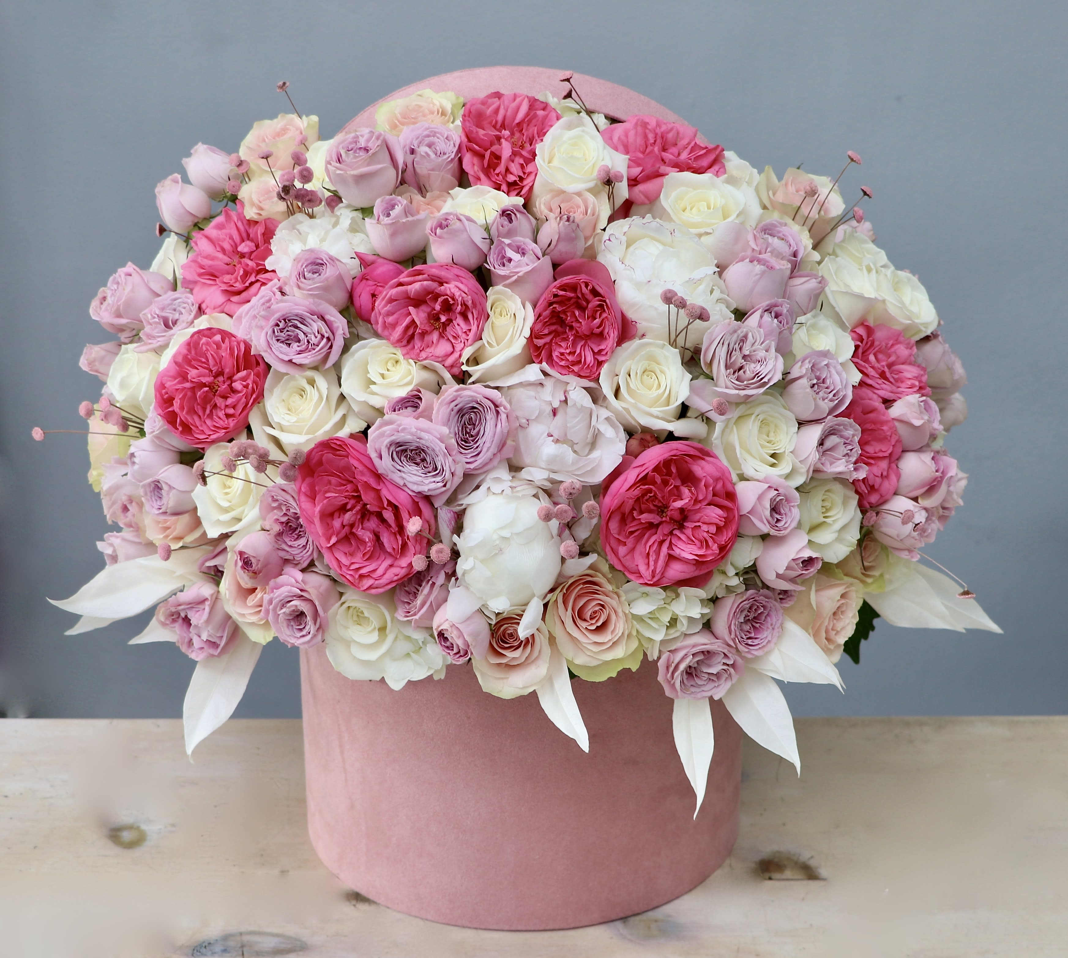 Dense arrangement of pink and white roses and peonies in a round pink hatbox container