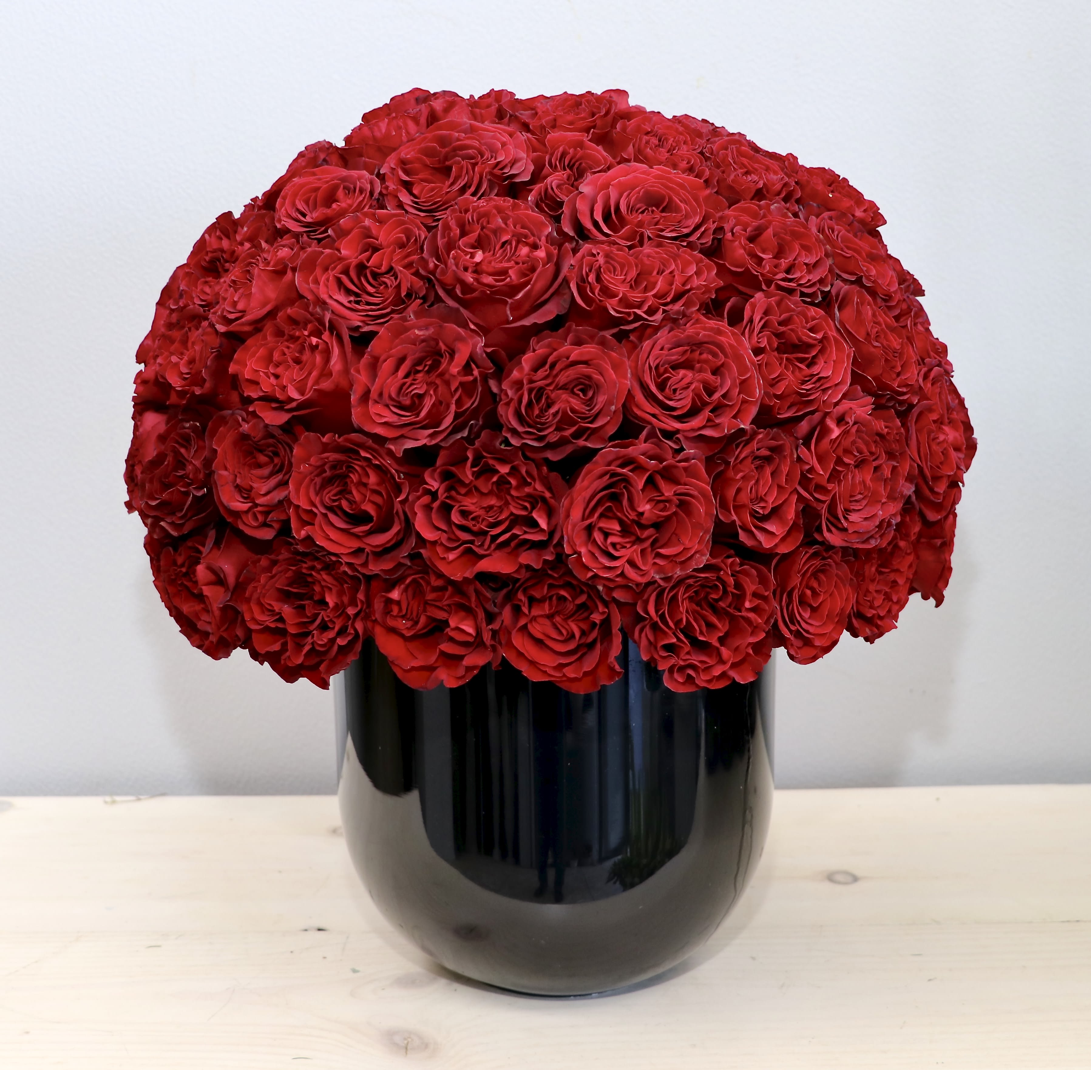 Dense dome of red roses arranged tightly in a glossy black cylindrical vase